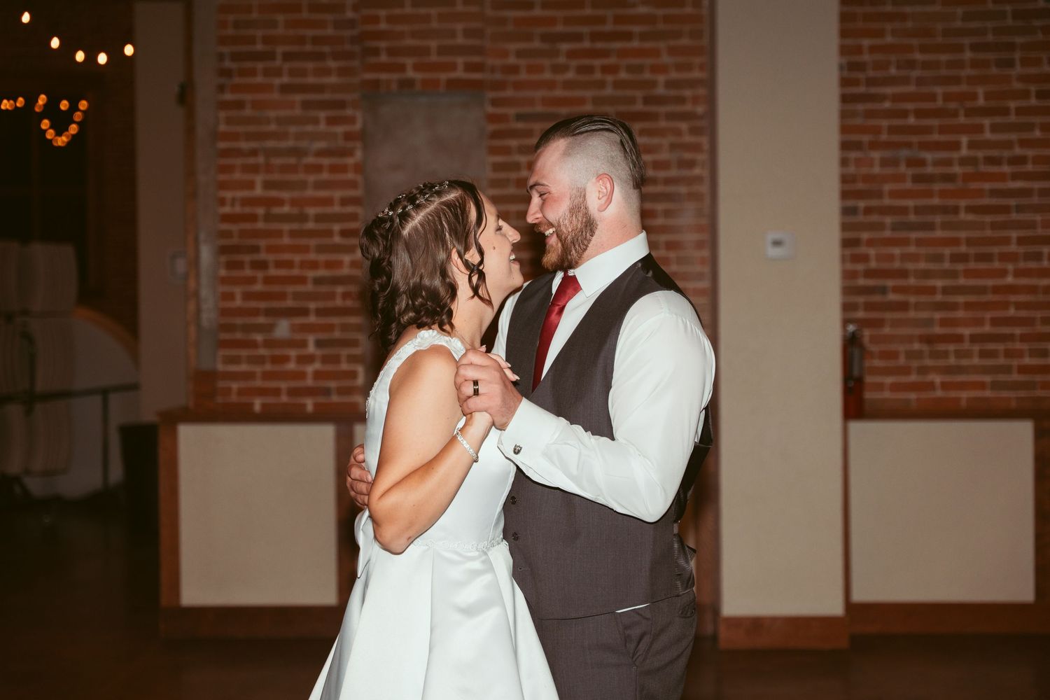 A couple shares a romantic moment while dancing in a rustic venue with string lights.