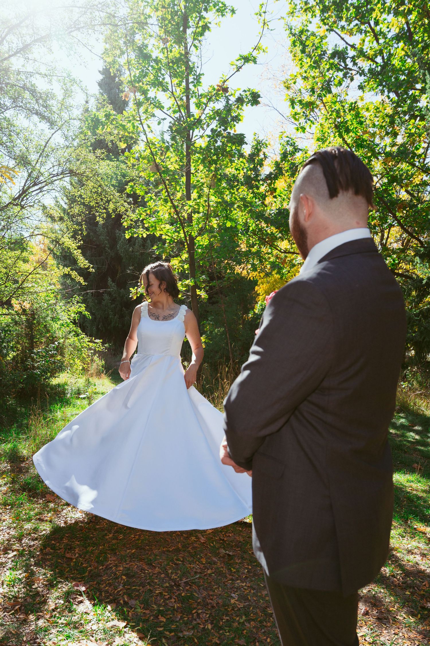 Bride in flowing white dress twirls in garden setting while groom watches.