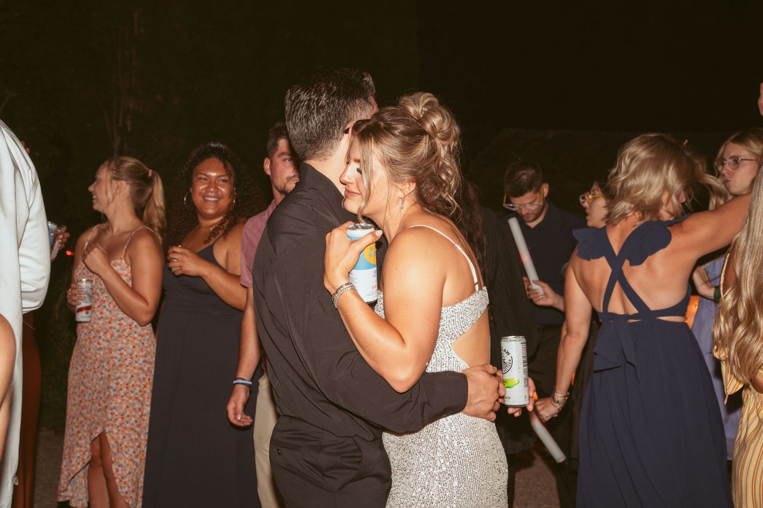 Wedding guests dancing and celebrating on a dimly lit dance floor.