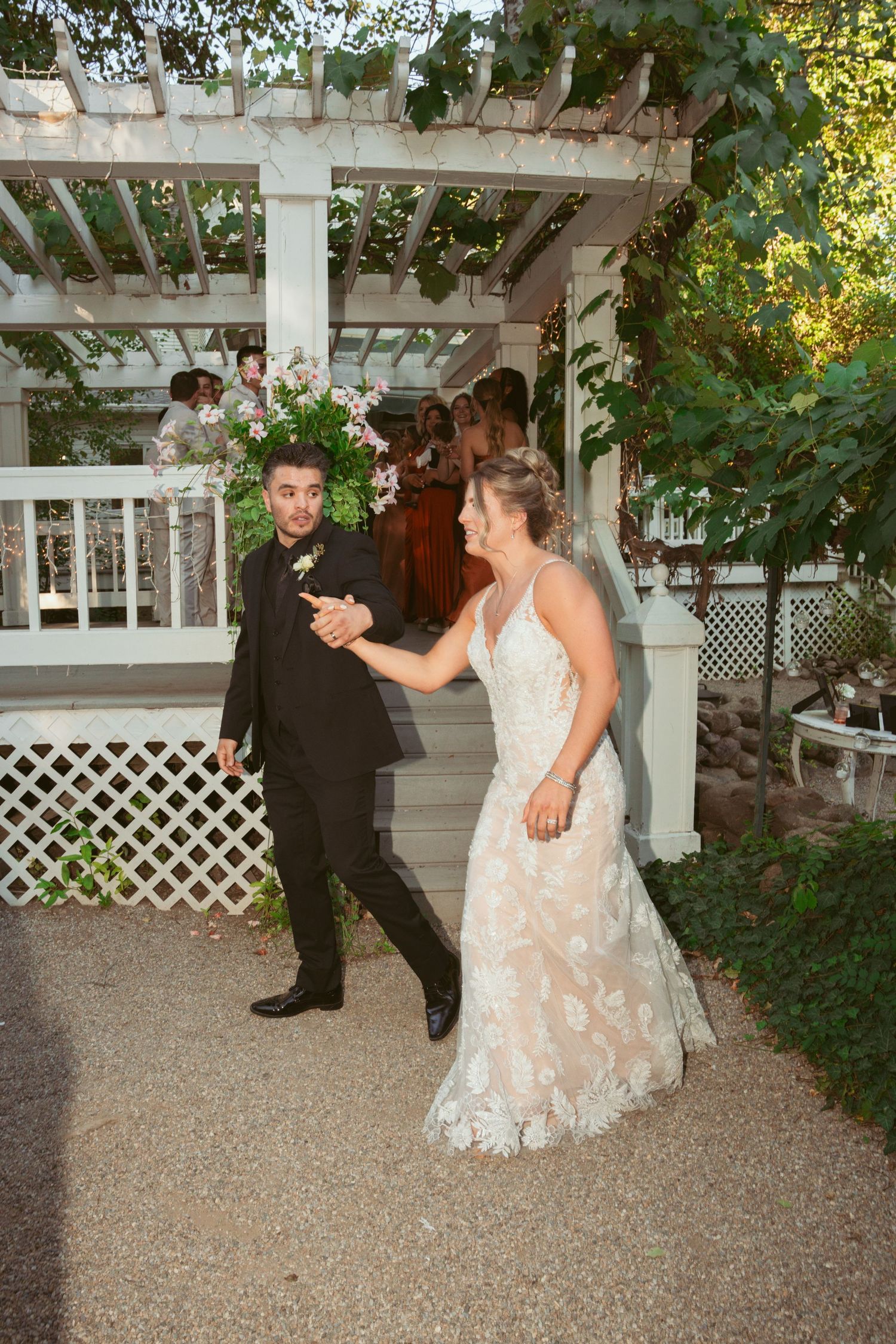 A couple dancing together under a garden pergola decorated with flowers and greenery.