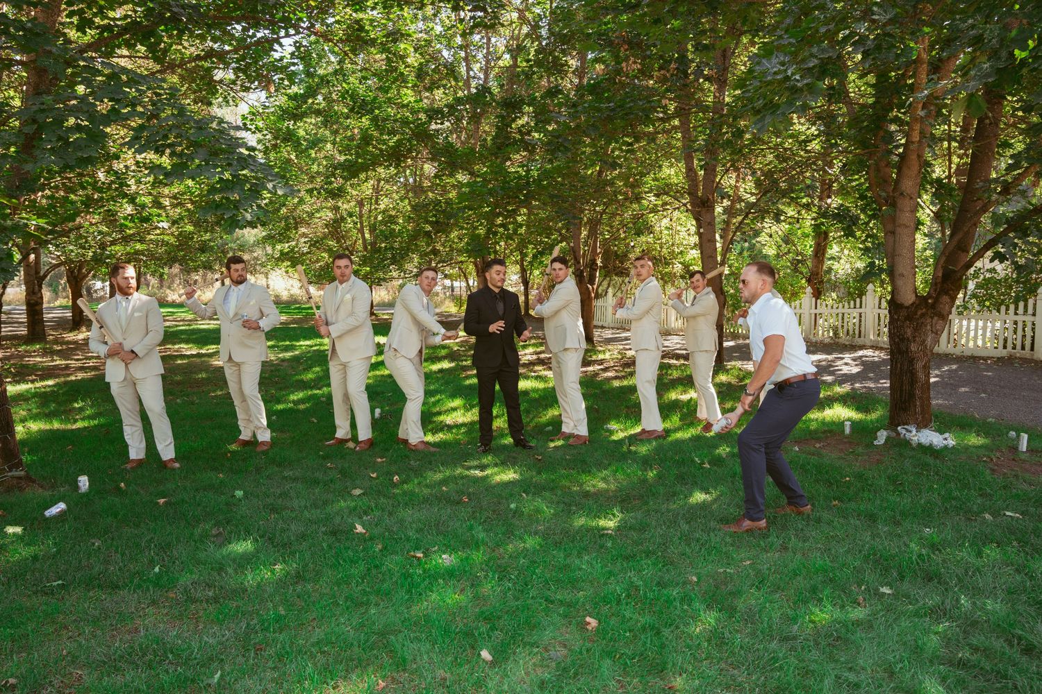 Wedding party members in light colored suits line up for photos in a garden setting.