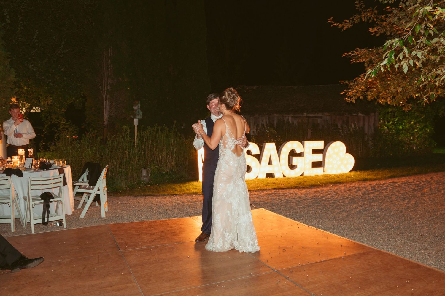 Wedding guests dance and celebrate on an outdoor dance floor at night with illuminated decor.