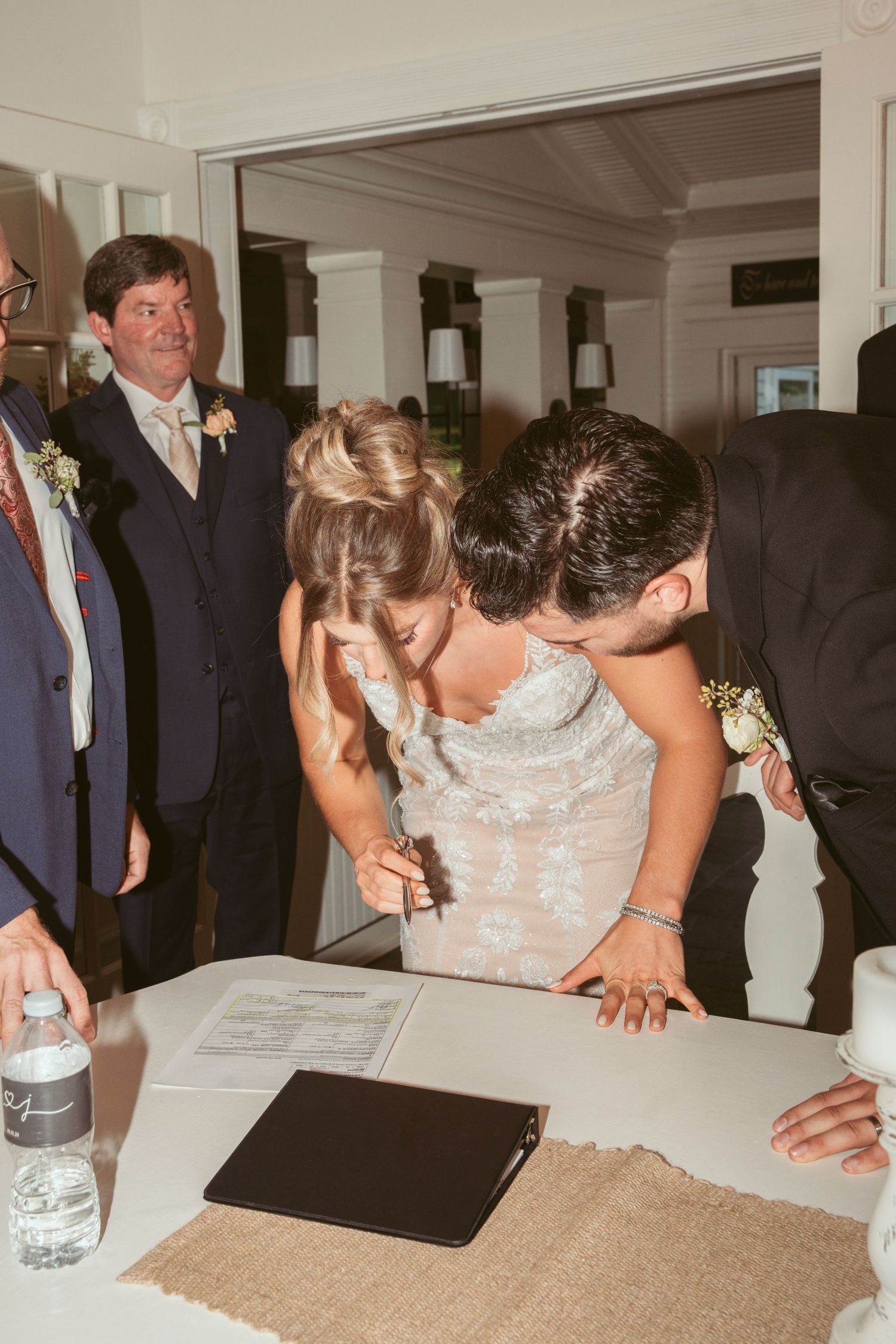 Wedding guests gather around a table during an indoor reception celebration.