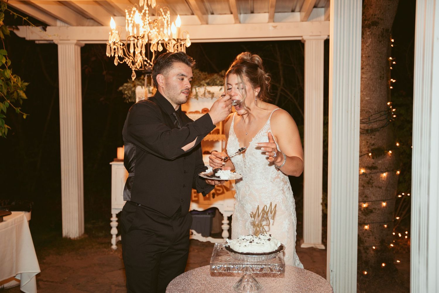 Elegant wedding reception setup with white columns, chandeliers, and wooden beams overhead.
