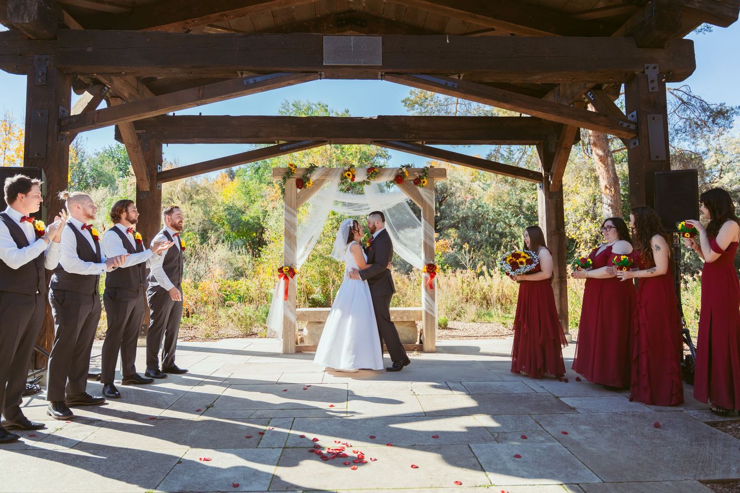 Wide angle shot of wedding party members gathered under an outdoor stone pavilion.