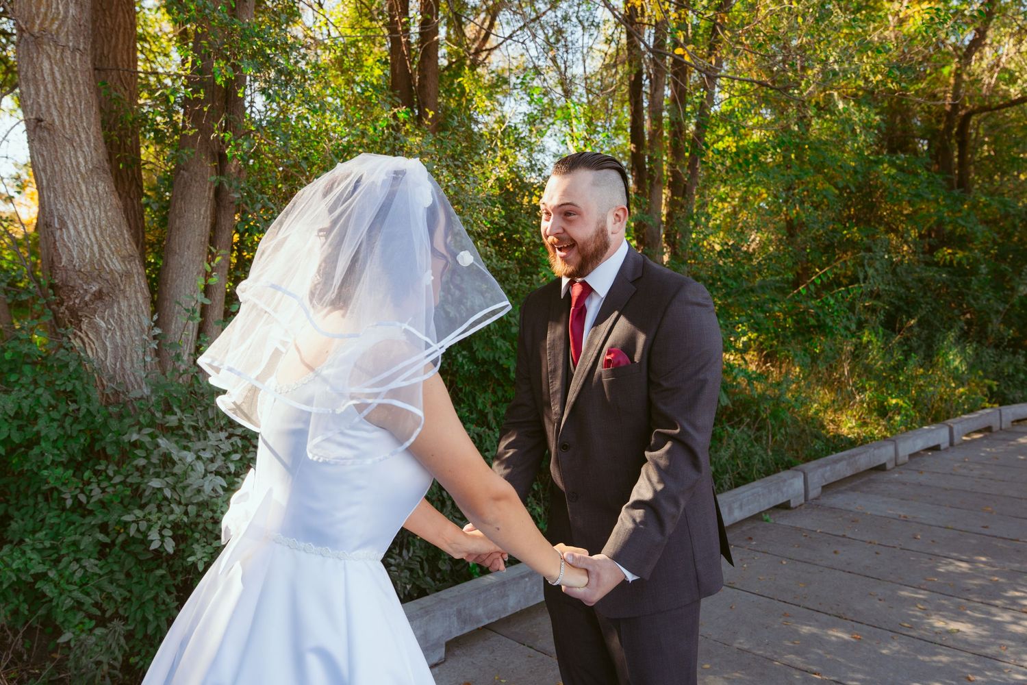 A couple shares a joyful moment on a wooden deck surrounded by trees.