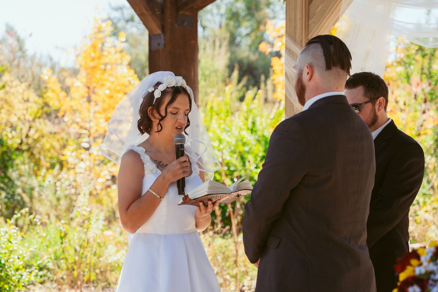 Wedding ceremony exchange of vows under rustic wooden pavilion with natural lighting.