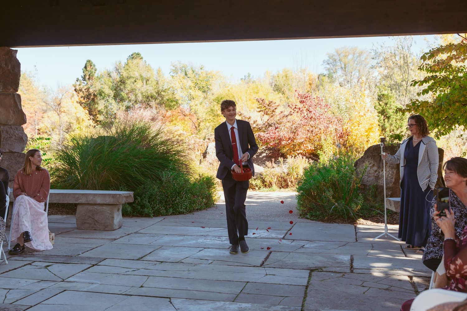 People gather on an outdoor stone patio surrounded by autumn foliage.