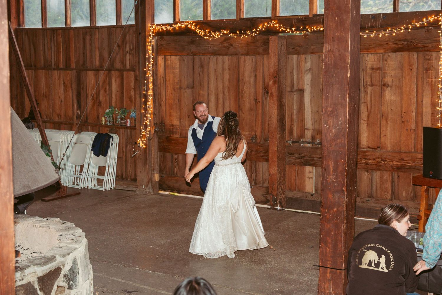 A festive dance scene unfolds in a wooden barn decorated with lights.