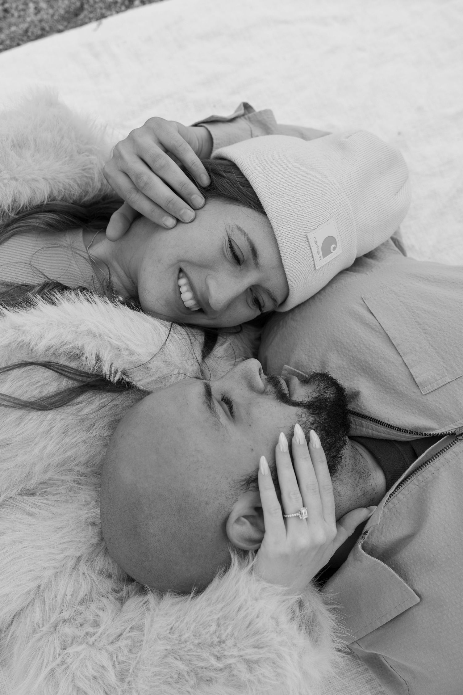 Intimate black and white portrait of couple lying close together on soft white fur.