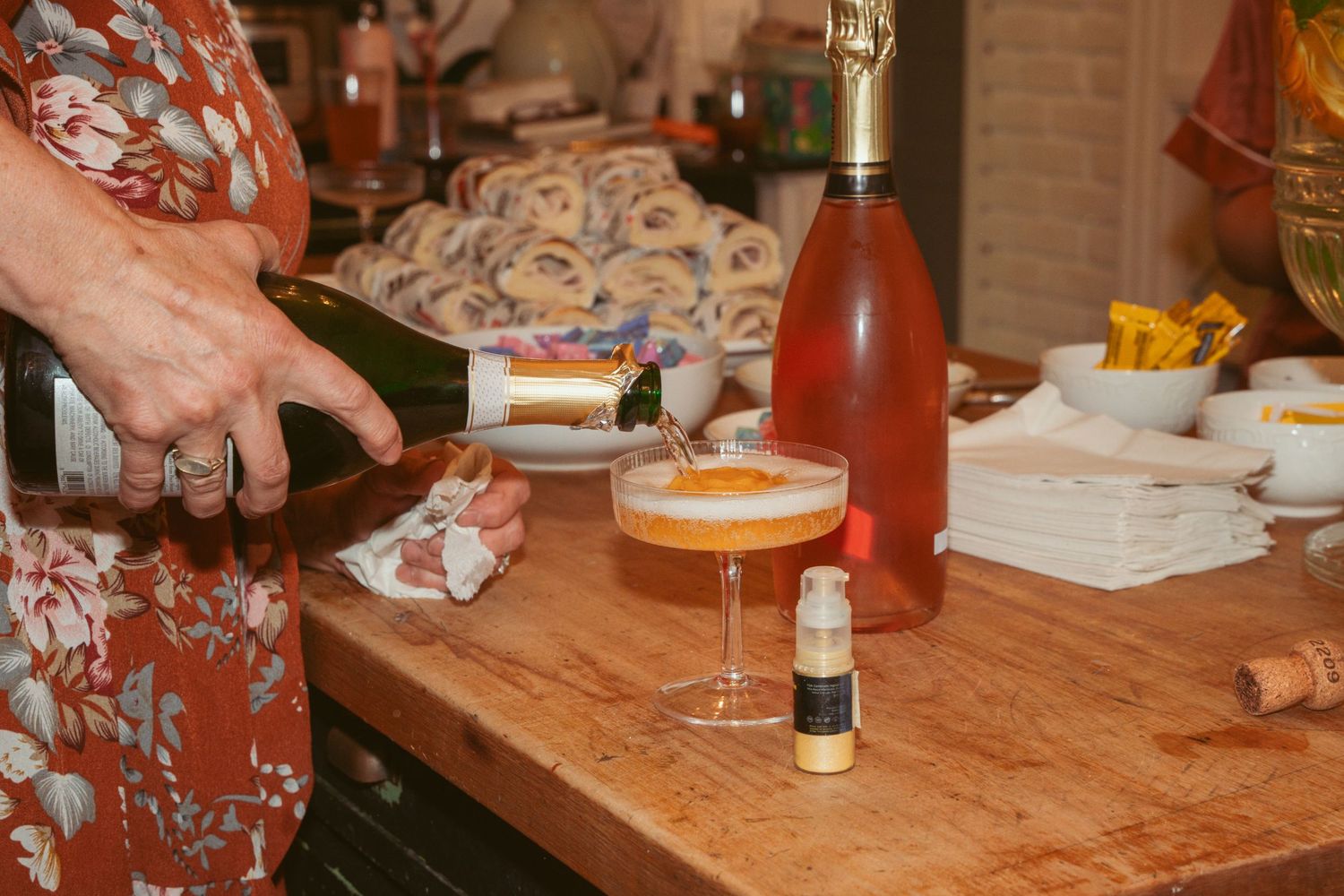Close-up of hands pouring cocktails on wooden counter with rose wine bottle.