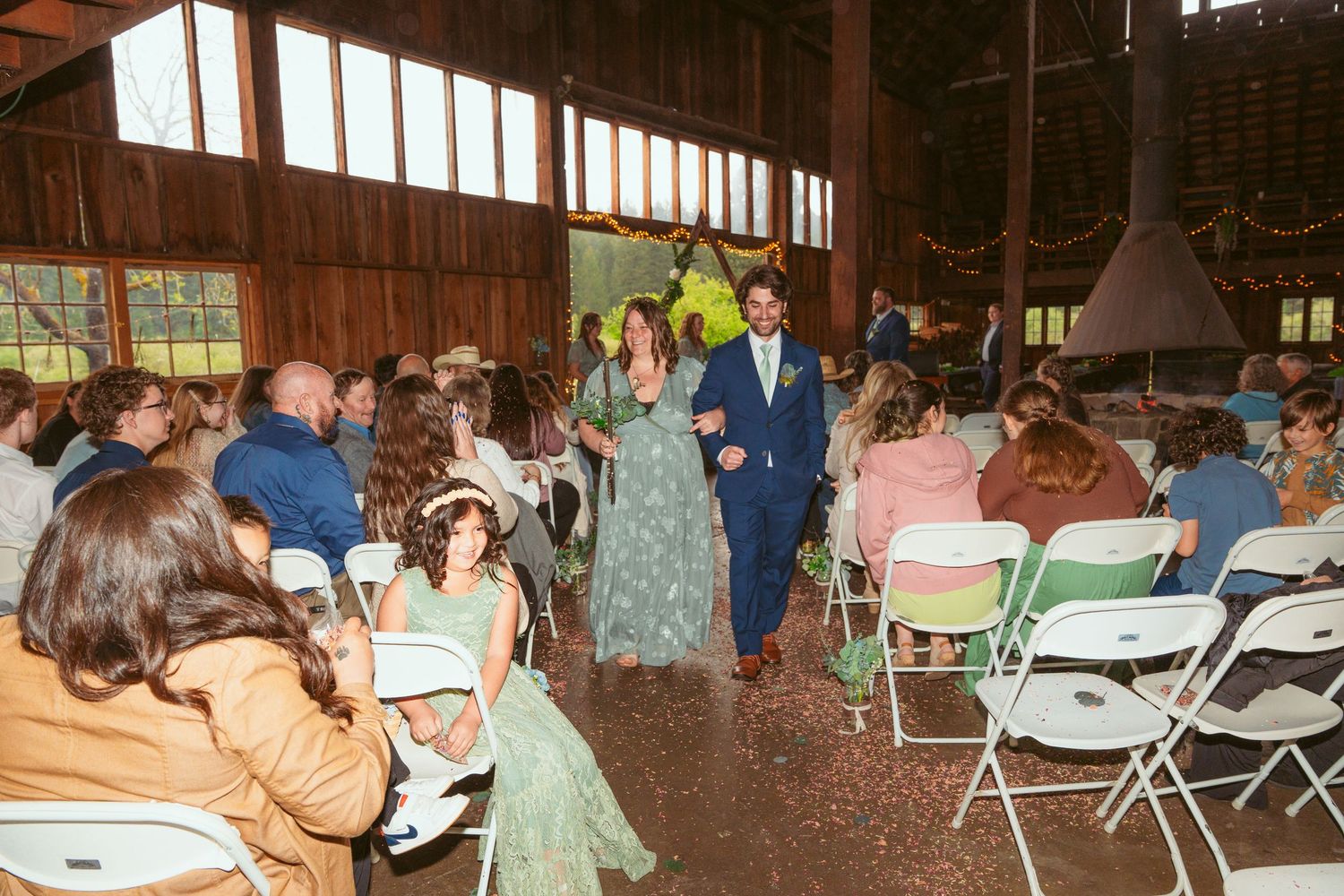 Rustic barn wedding venue filled with guests in white folding chairs.