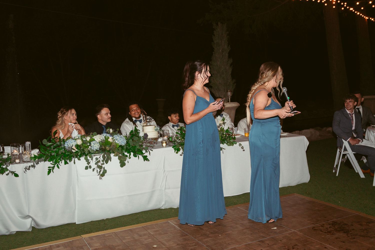 Evening wedding reception with string lights and guests dancing on a wooden dance floor.