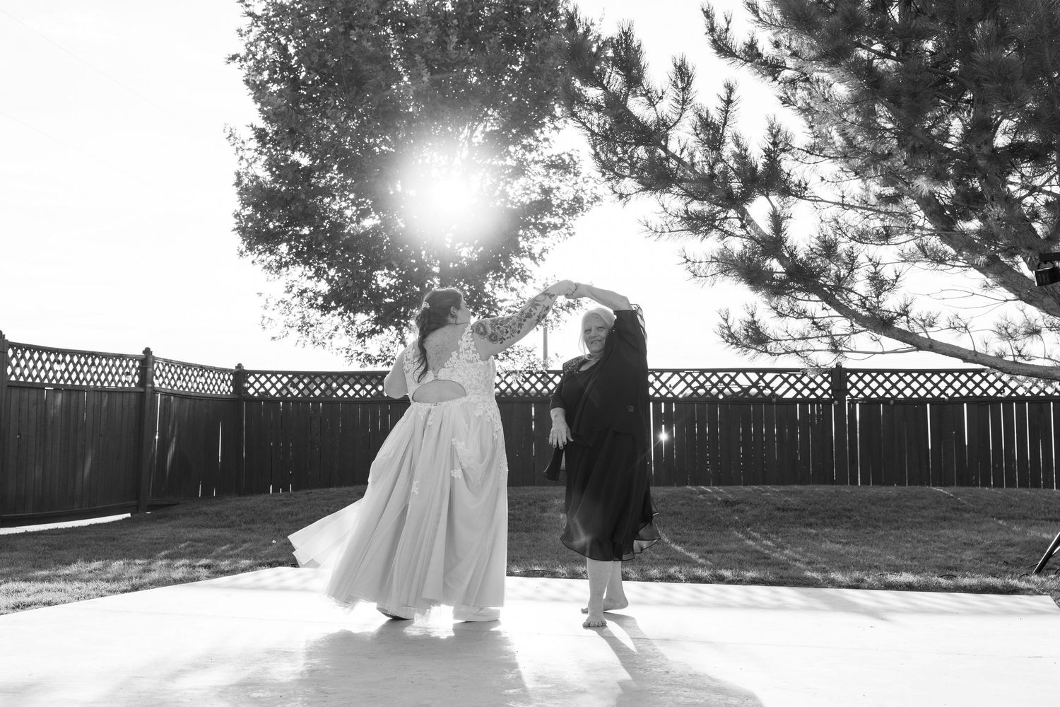 Black and white photo of a couple dancing outdoors with sunlight streaming through trees.