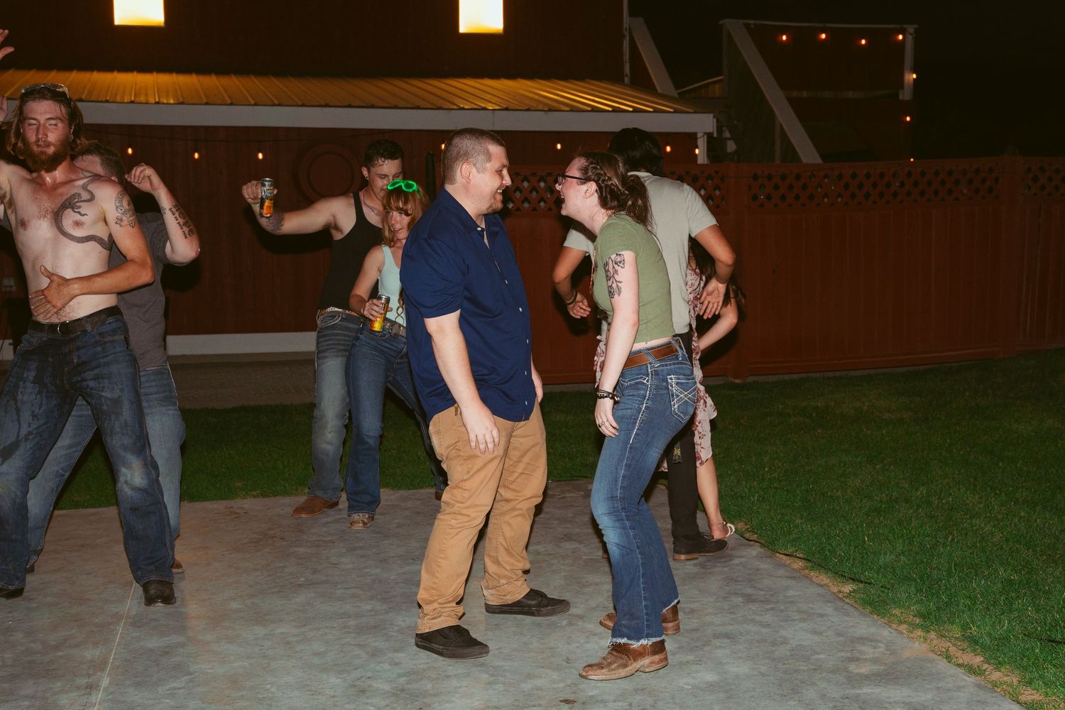 Wedding guests dancing in a line formation outside during evening reception.
