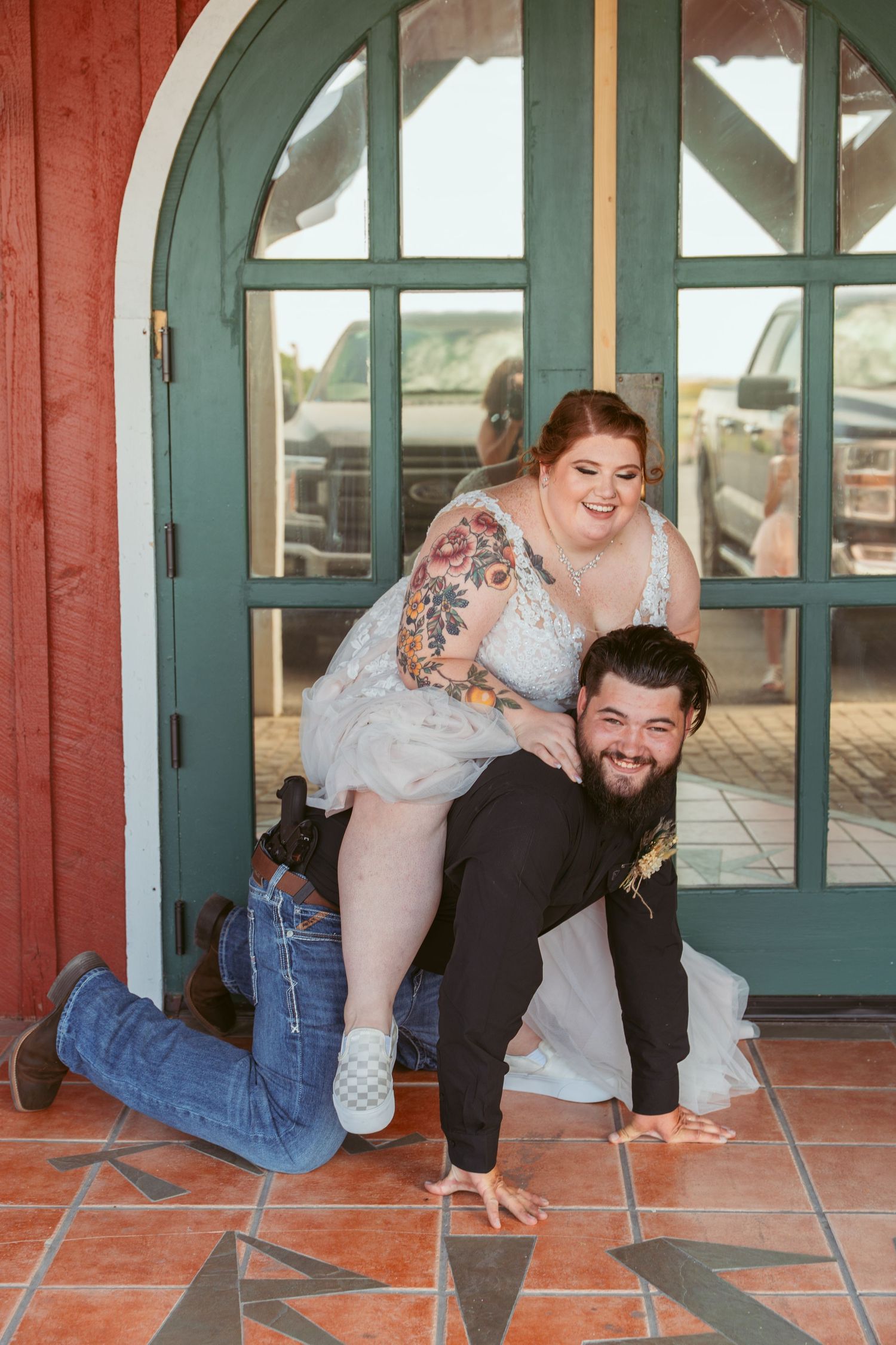 Fun wedding party poses playfully on red building porch with teal arched doors.