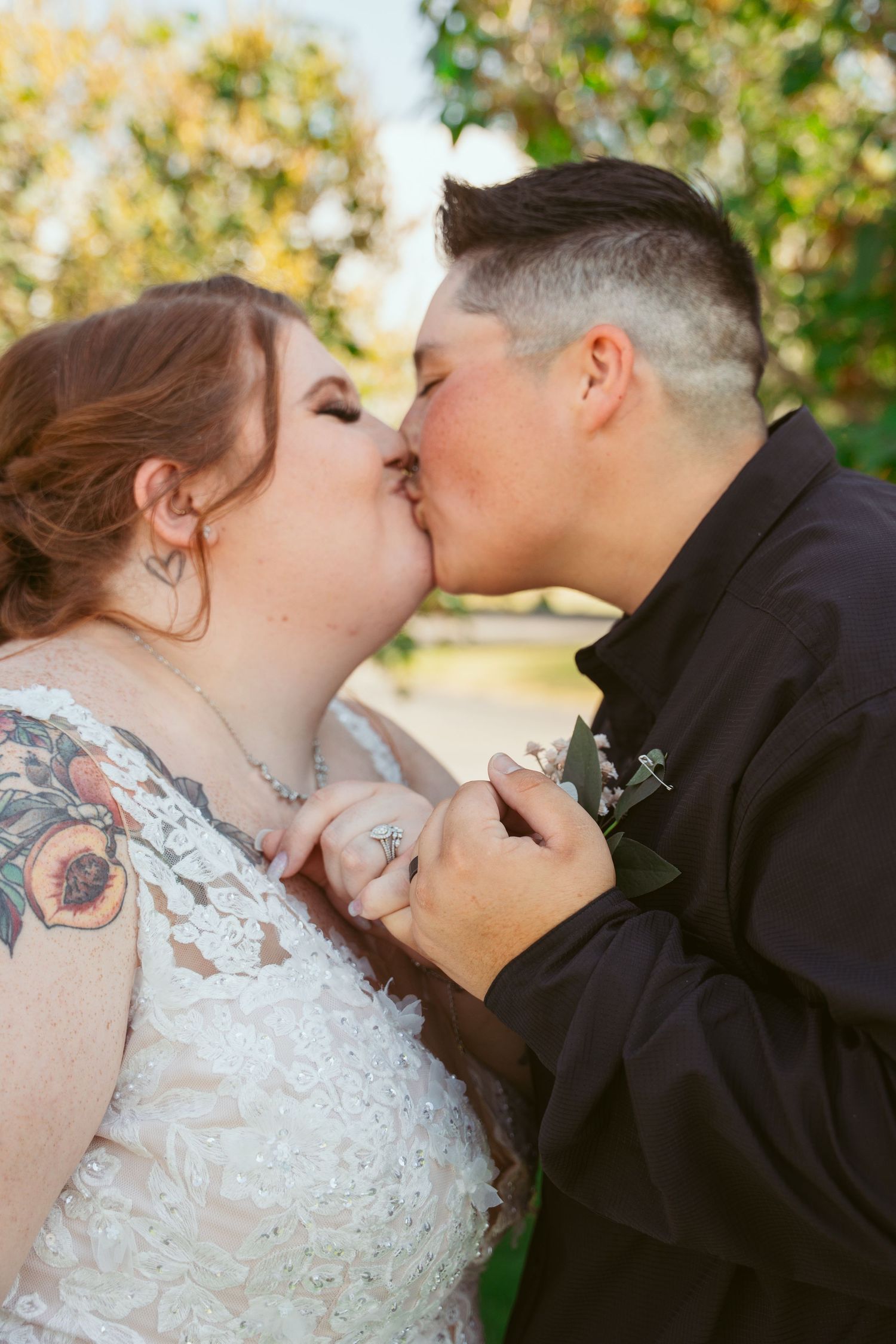 A couple shares a romantic kiss during their wedding ceremony, with autumn foliage in the background.