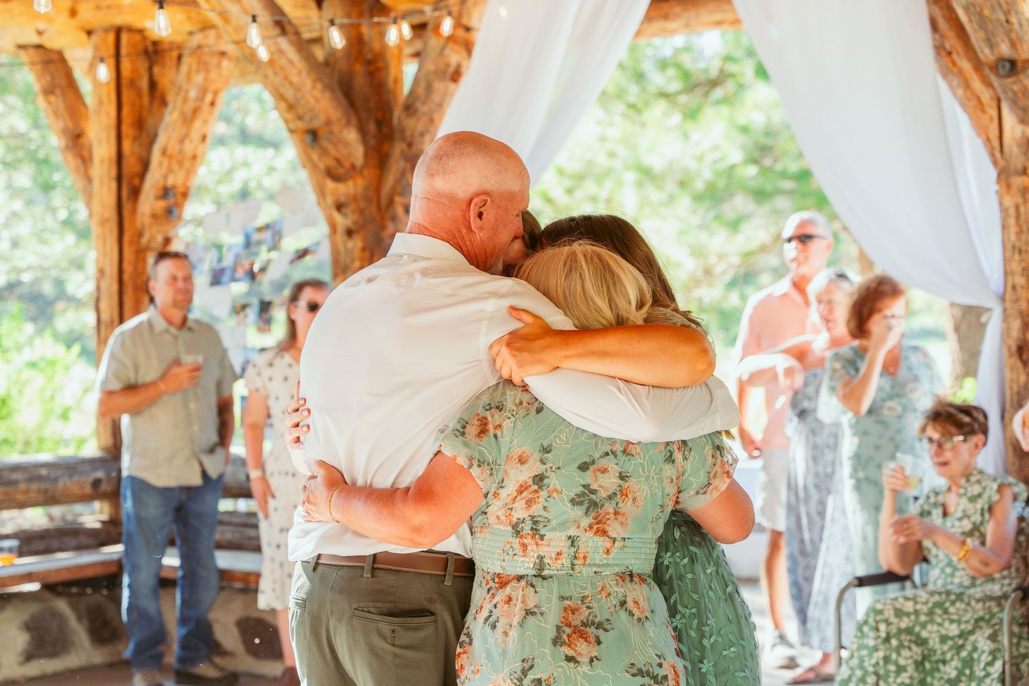 Dancing couple surrounded by guests at an outdoor wedding venue with timber frame construction.