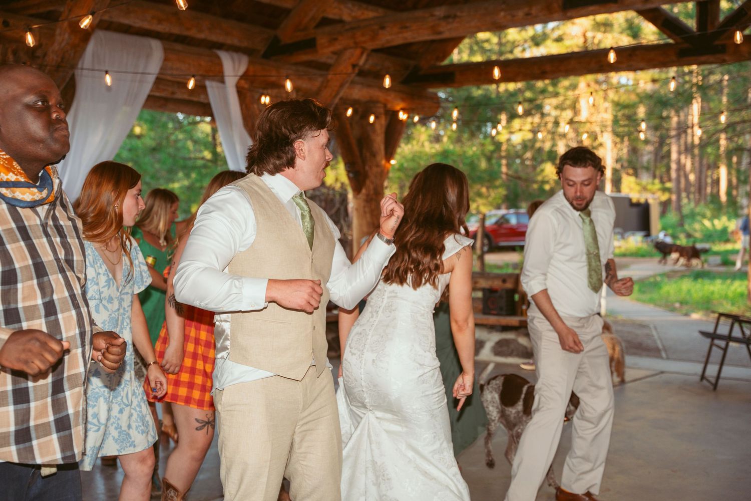 Wedding celebration with couples dancing under a wooden pavilion at sunset.