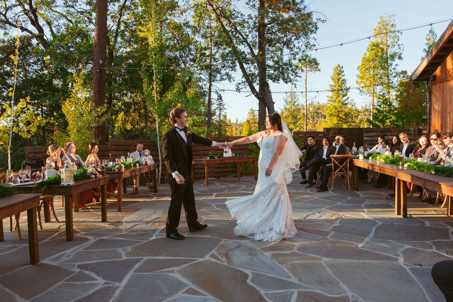 Couple performs romantic dance on stone patio with rustic wooden fencing and forest scenery.
