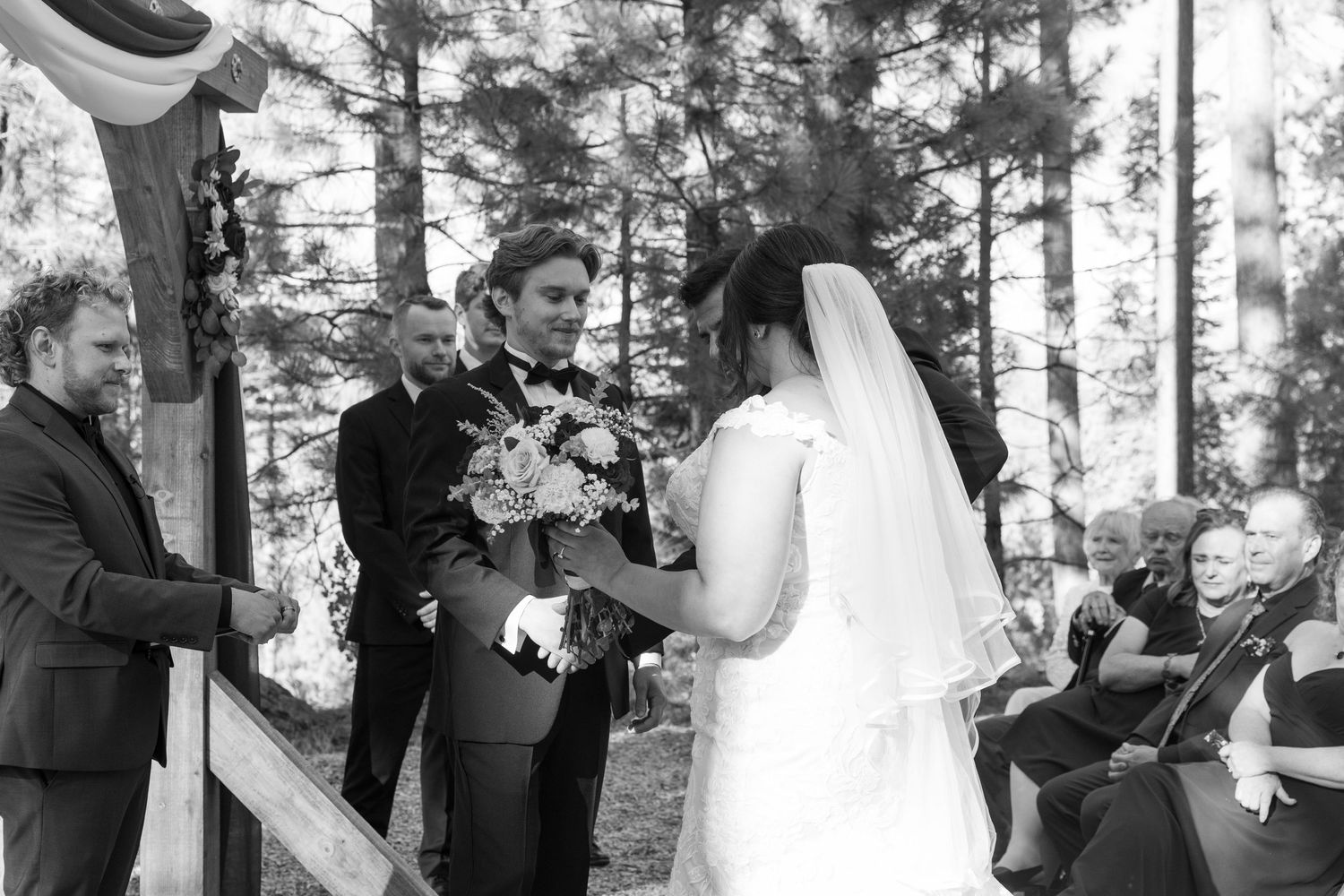 Wedding couple exchanges vows during an intimate forest ceremony under natural sunlight.