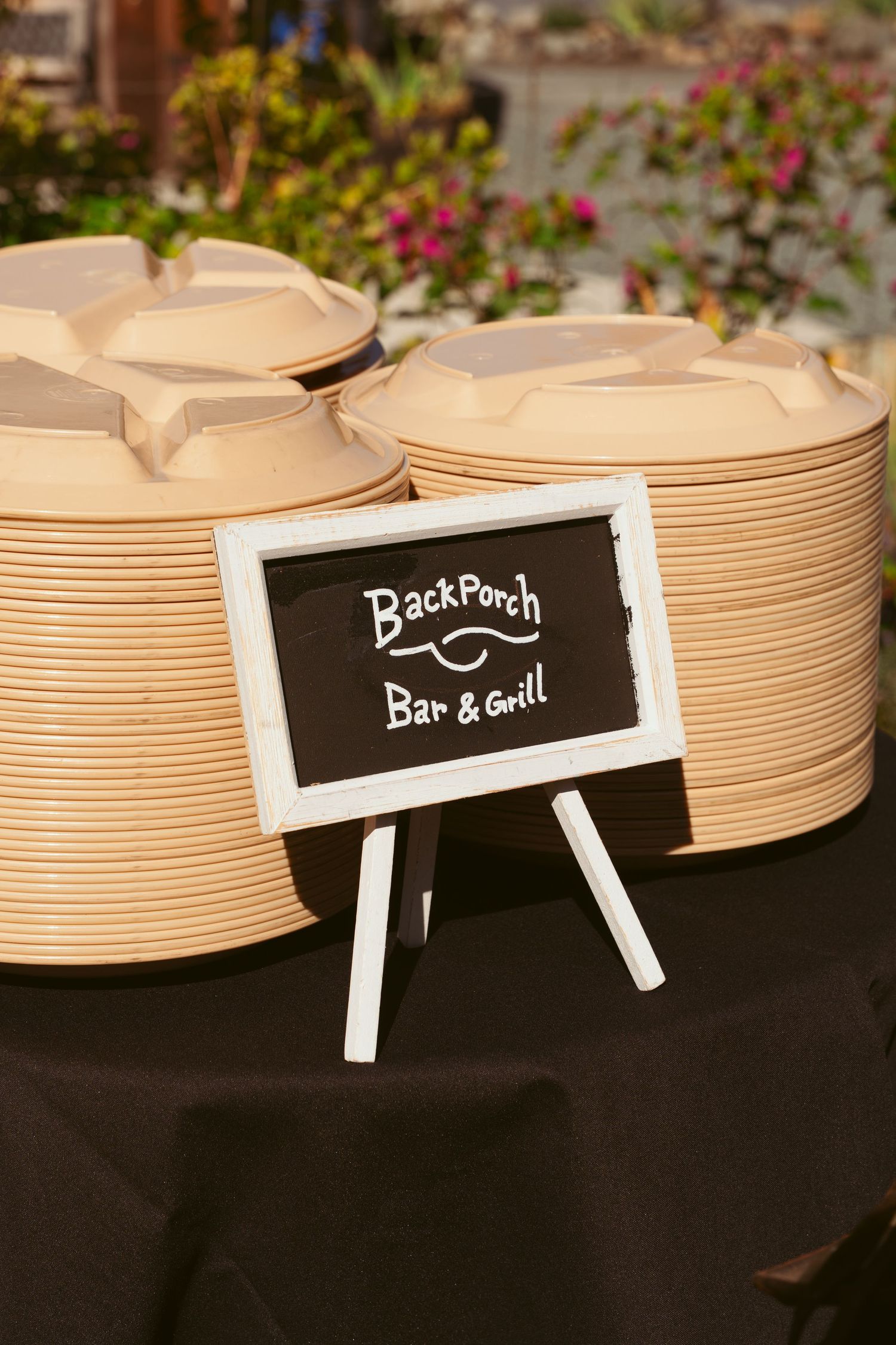 Stack of disposable plates with 'BackPorch Bar & Grill' chalkboard sign at catering station.