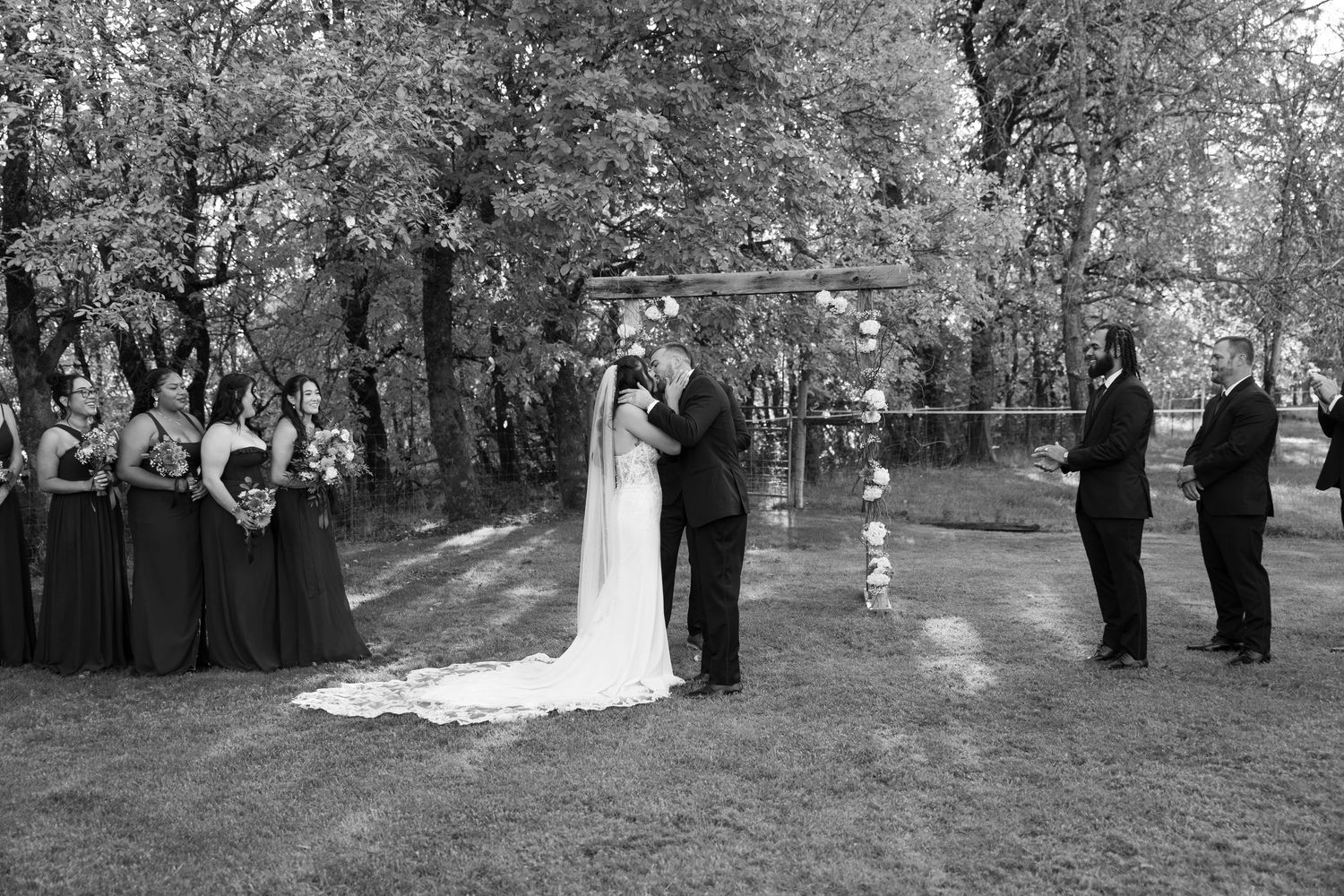Outdoor wedding ceremony in a wooded setting with bridesmaids in navy dresses and groomsmen standing on either side.