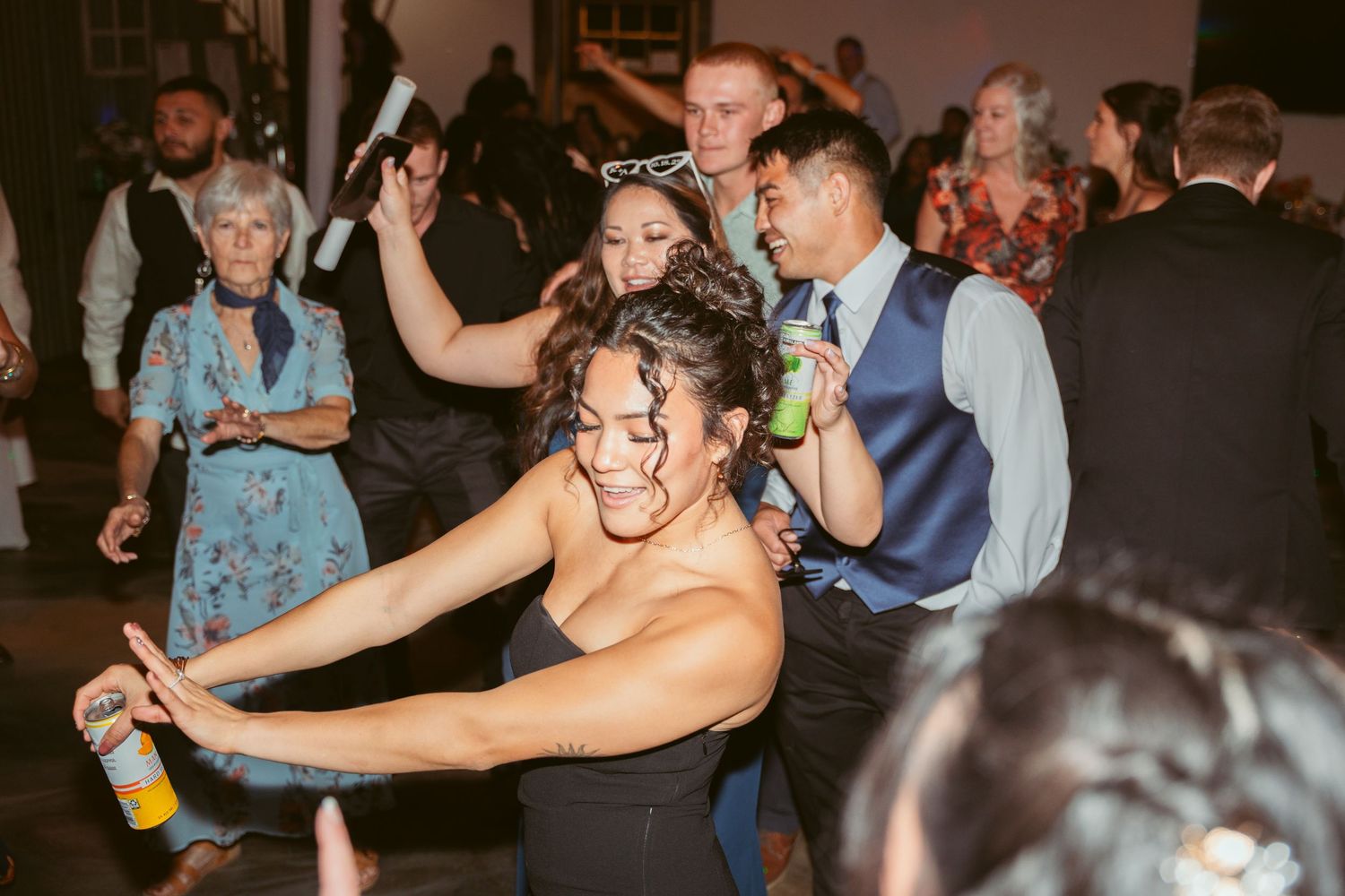 Partygoers dance and celebrate with drinks and glow sticks under string lights.