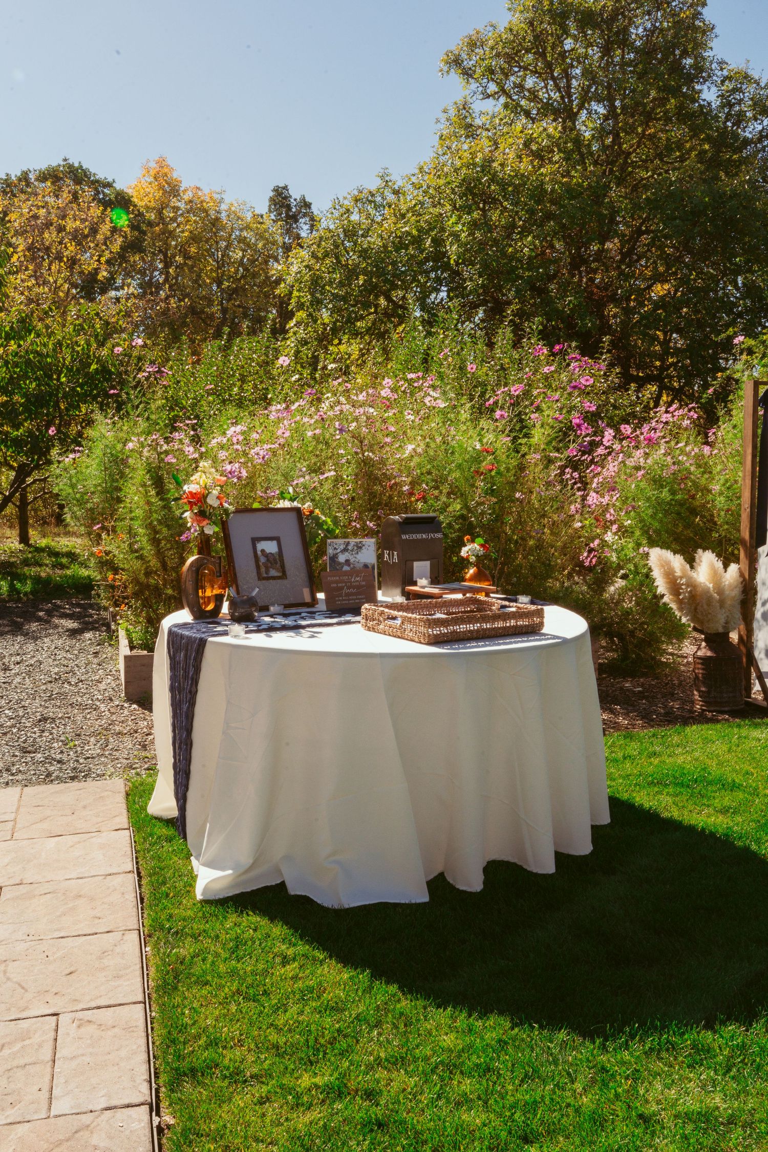 Elegant outdoor wedding display table with white tablecloth surrounded by blooming garden flowers.