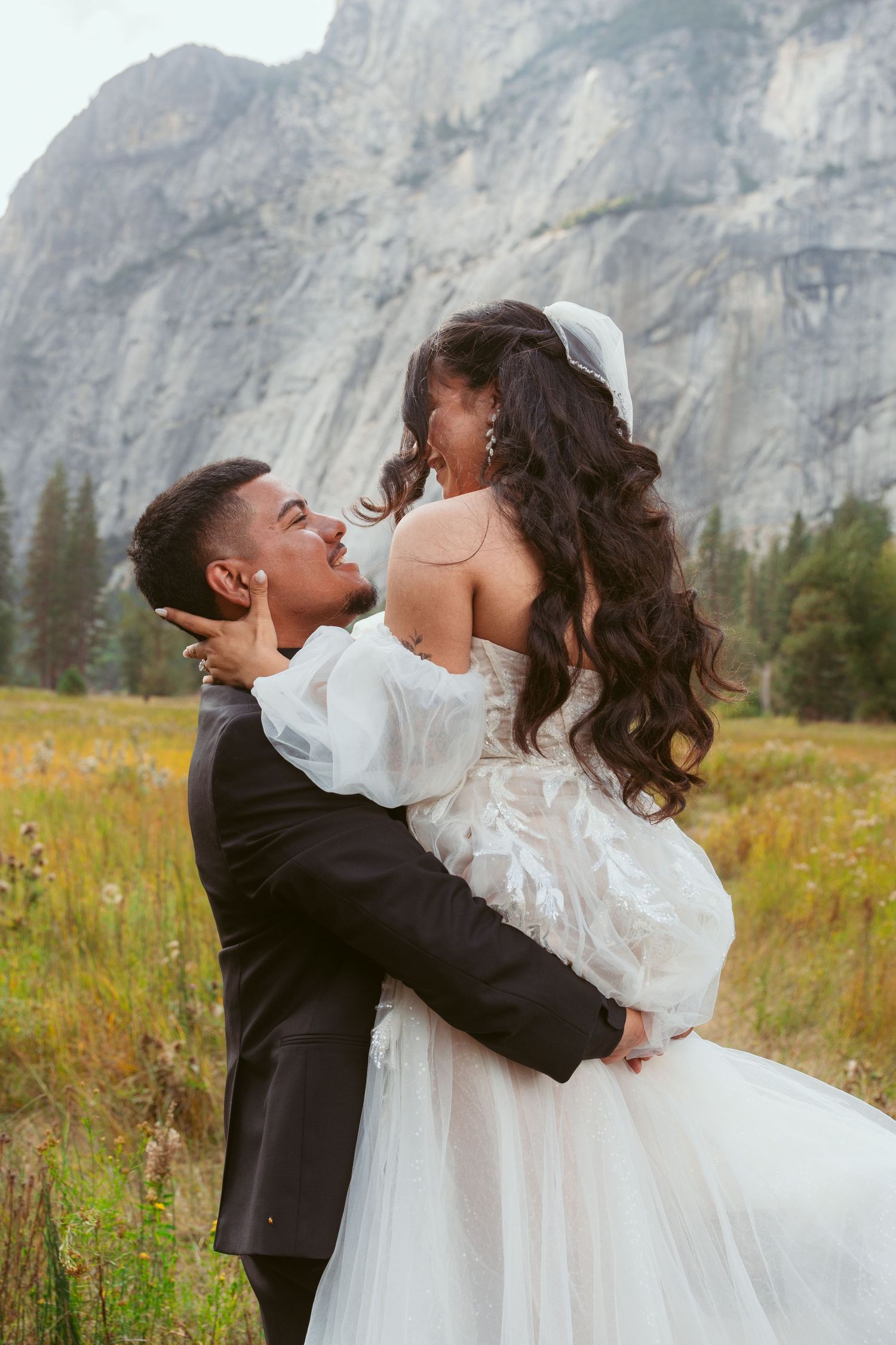 A romantic wedding portrait in a meadow with dramatic mountain cliffs in the background.