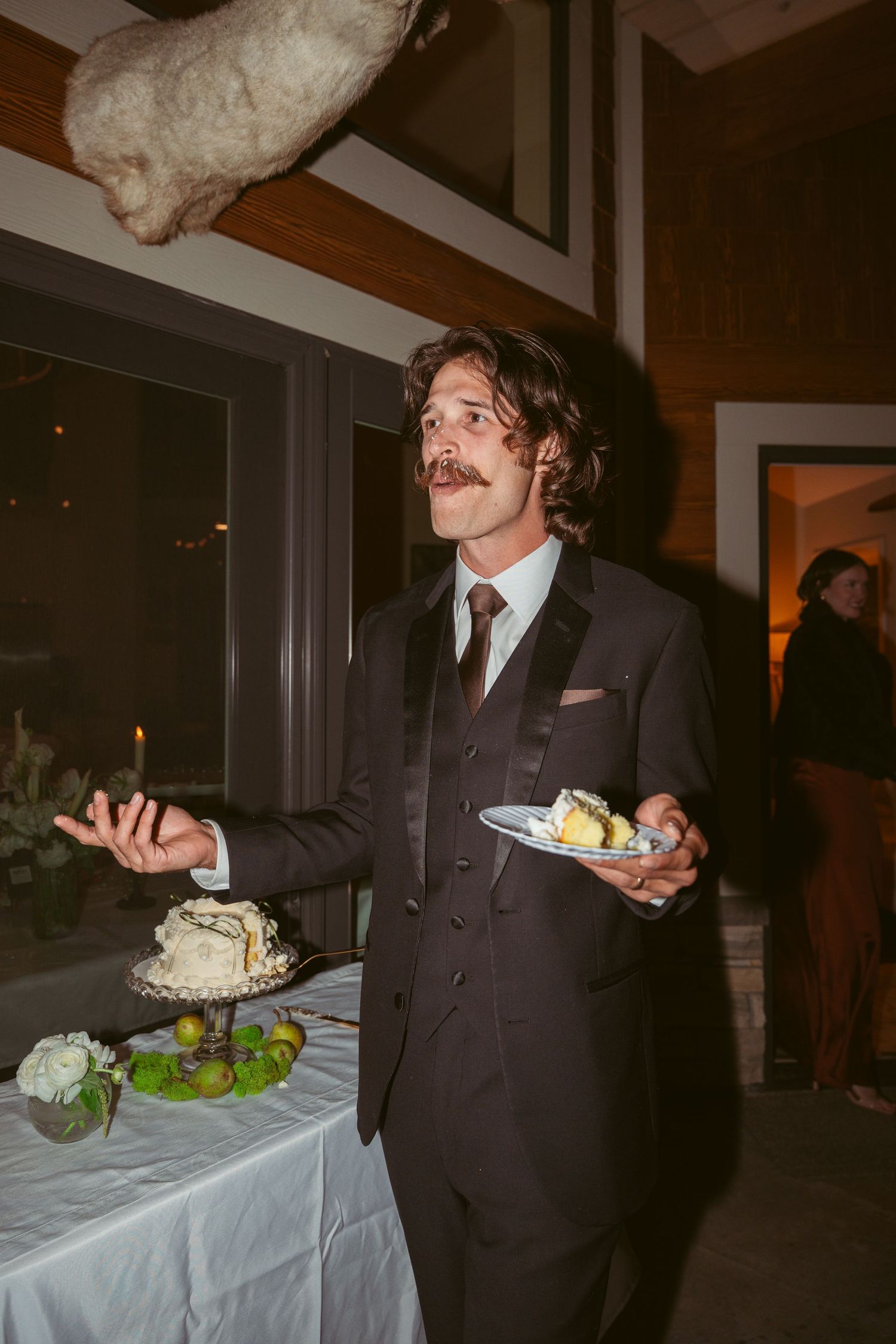 A groom in a dark suit enjoys cake during the wedding reception festivities.