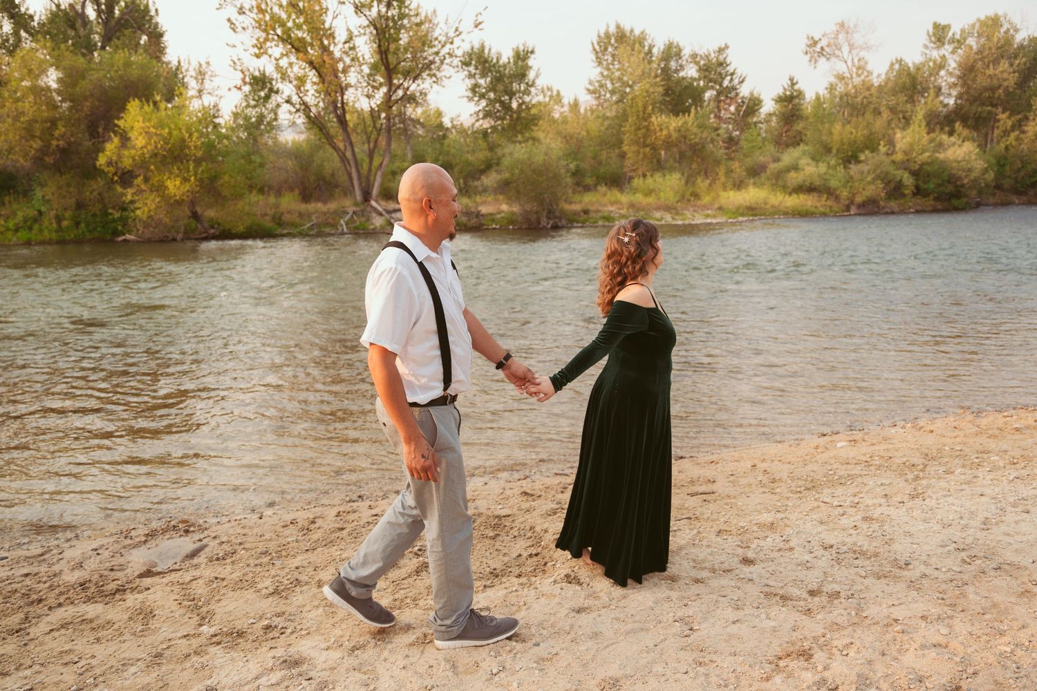 A couple walks hand in hand along a scenic waterfront path during sunset.