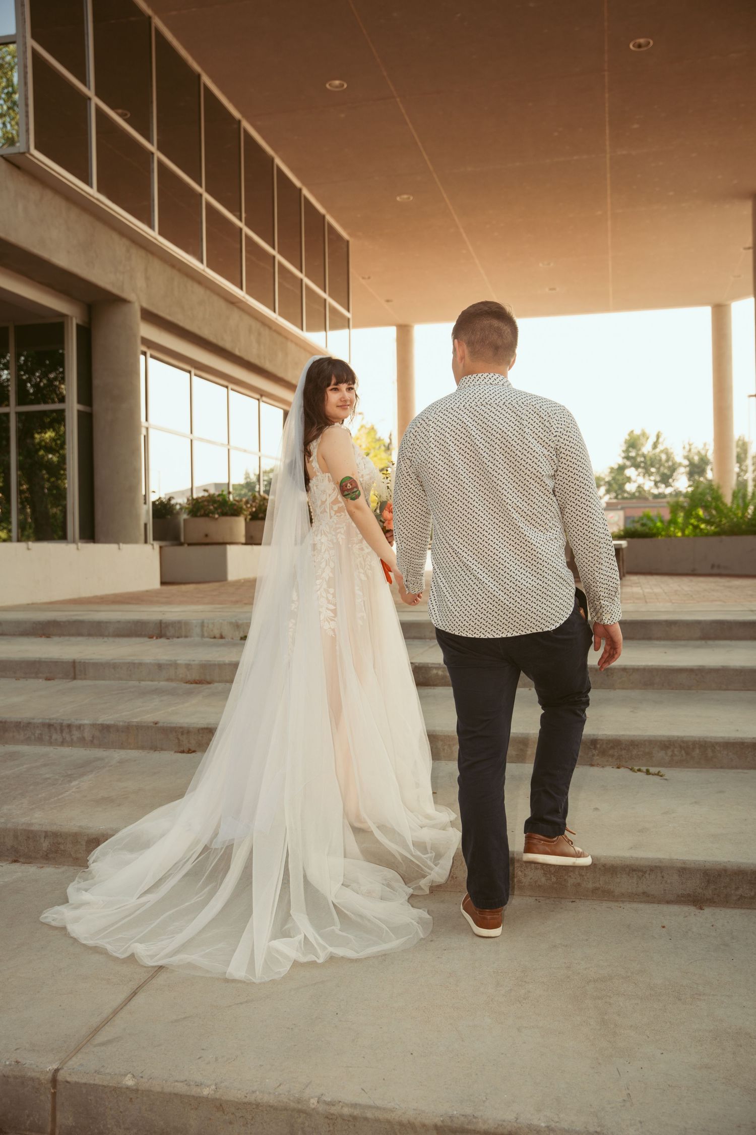 Wedding couple sitting on concrete steps in warm evening light.