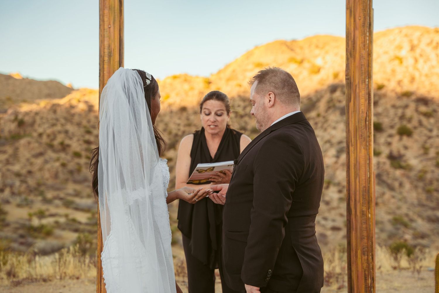 Intimate desert wedding ceremony with officiant and couple under wooden arch at golden hour.