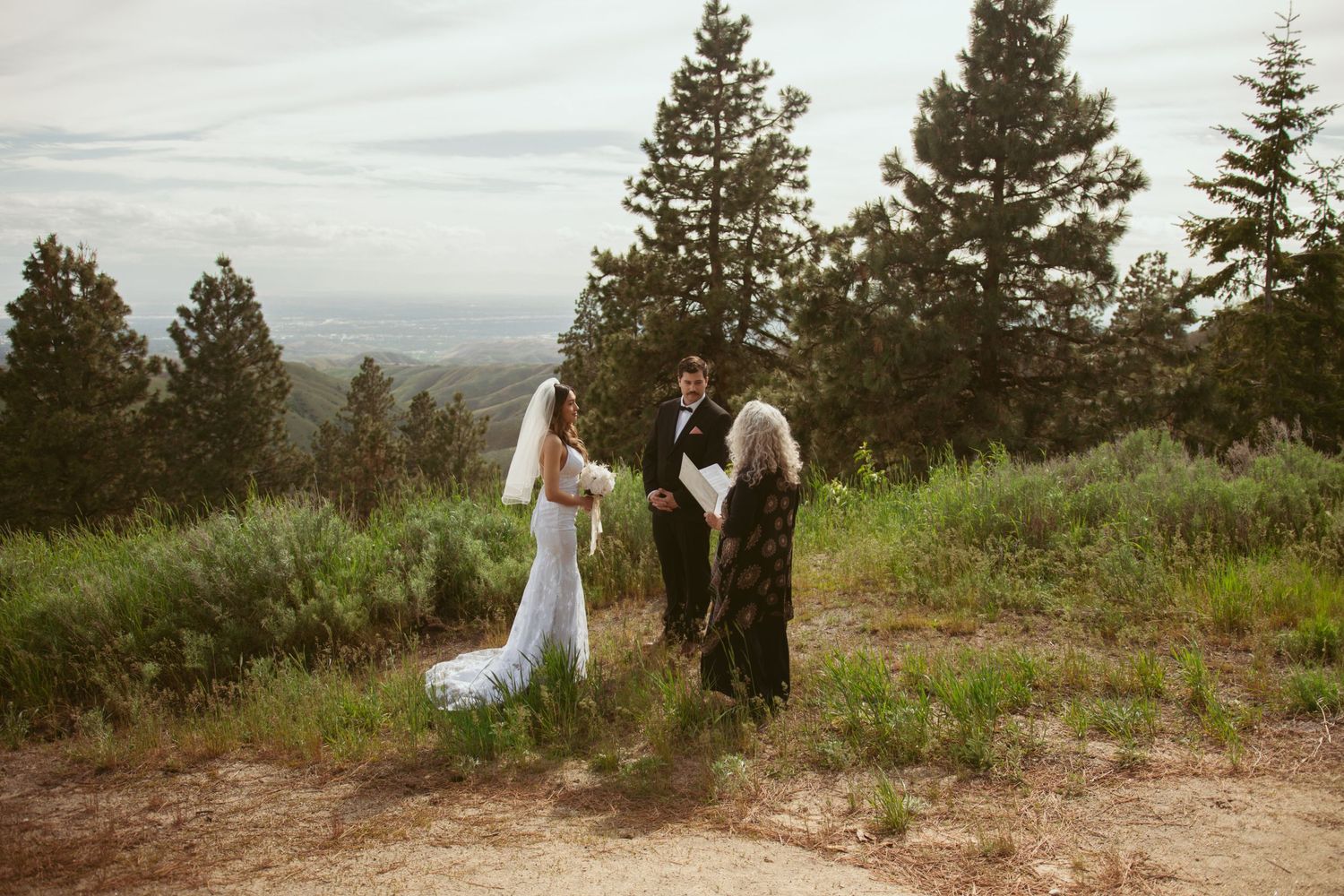 Wedding ceremony taking place on a scenic mountain overlook with evergreen trees.