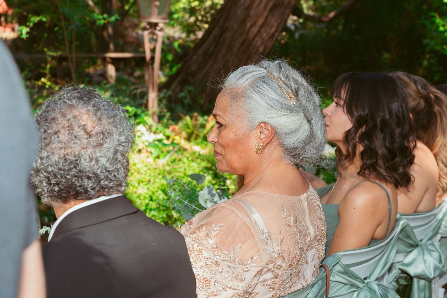 Festive outdoor wedding reception with guests dancing under trees and natural lighting.