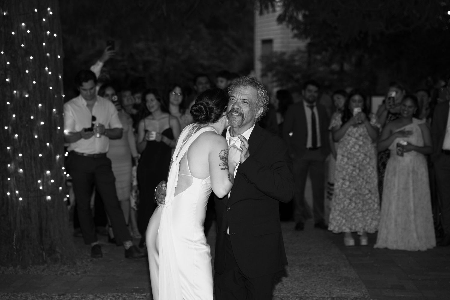 Black and white photo of couples dancing at a nighttime outdoor wedding celebration.