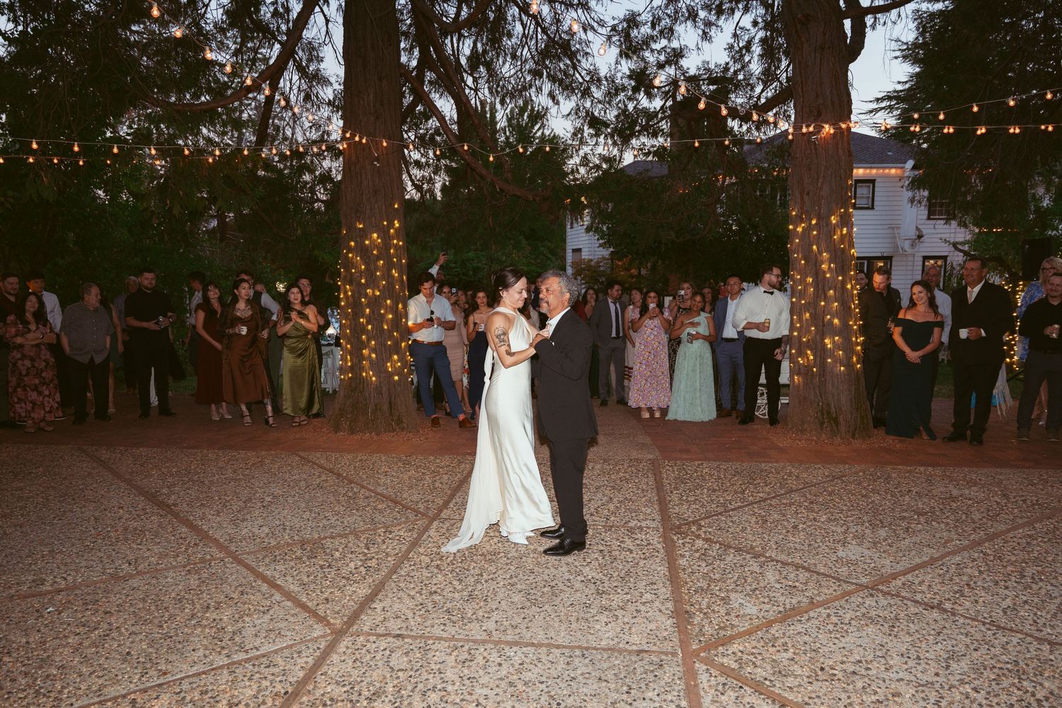 Couples dancing on an outdoor patio illuminated by overhead string lights at a wedding reception.