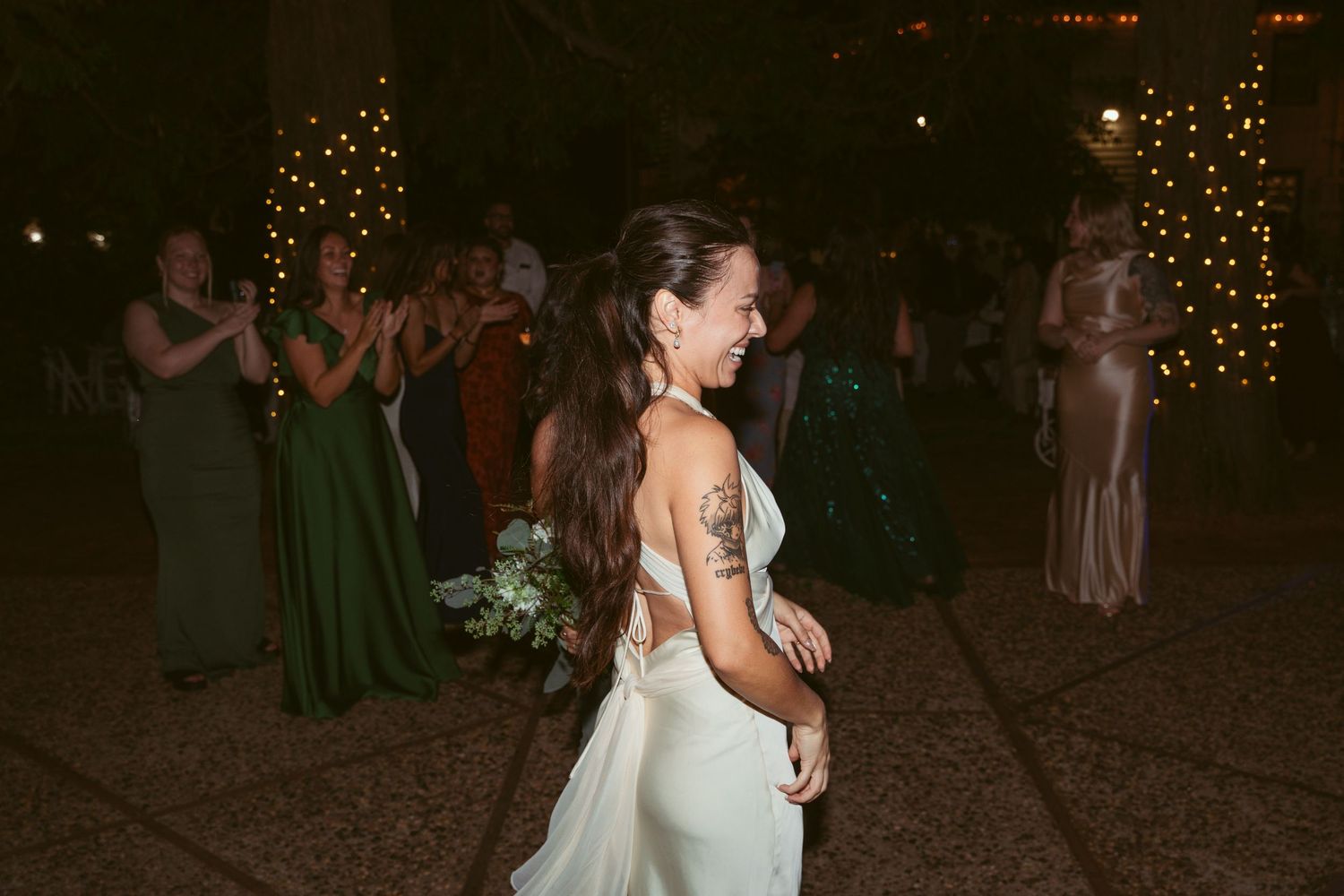 Couples dancing together at a nighttime wedding reception under glowing string lights.
