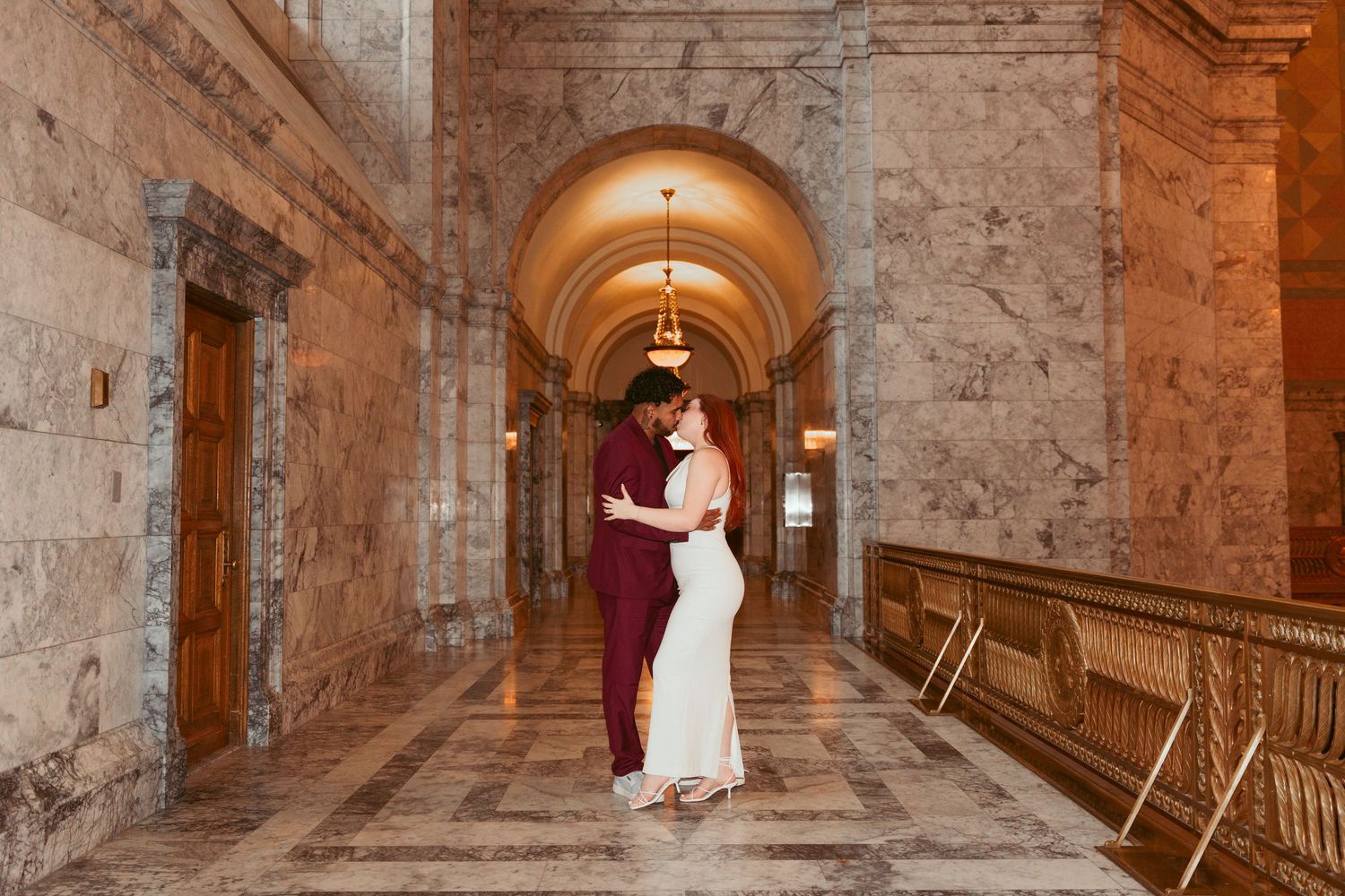 A tender embrace in a historic marble corridor with arched ceilings and warm lighting.