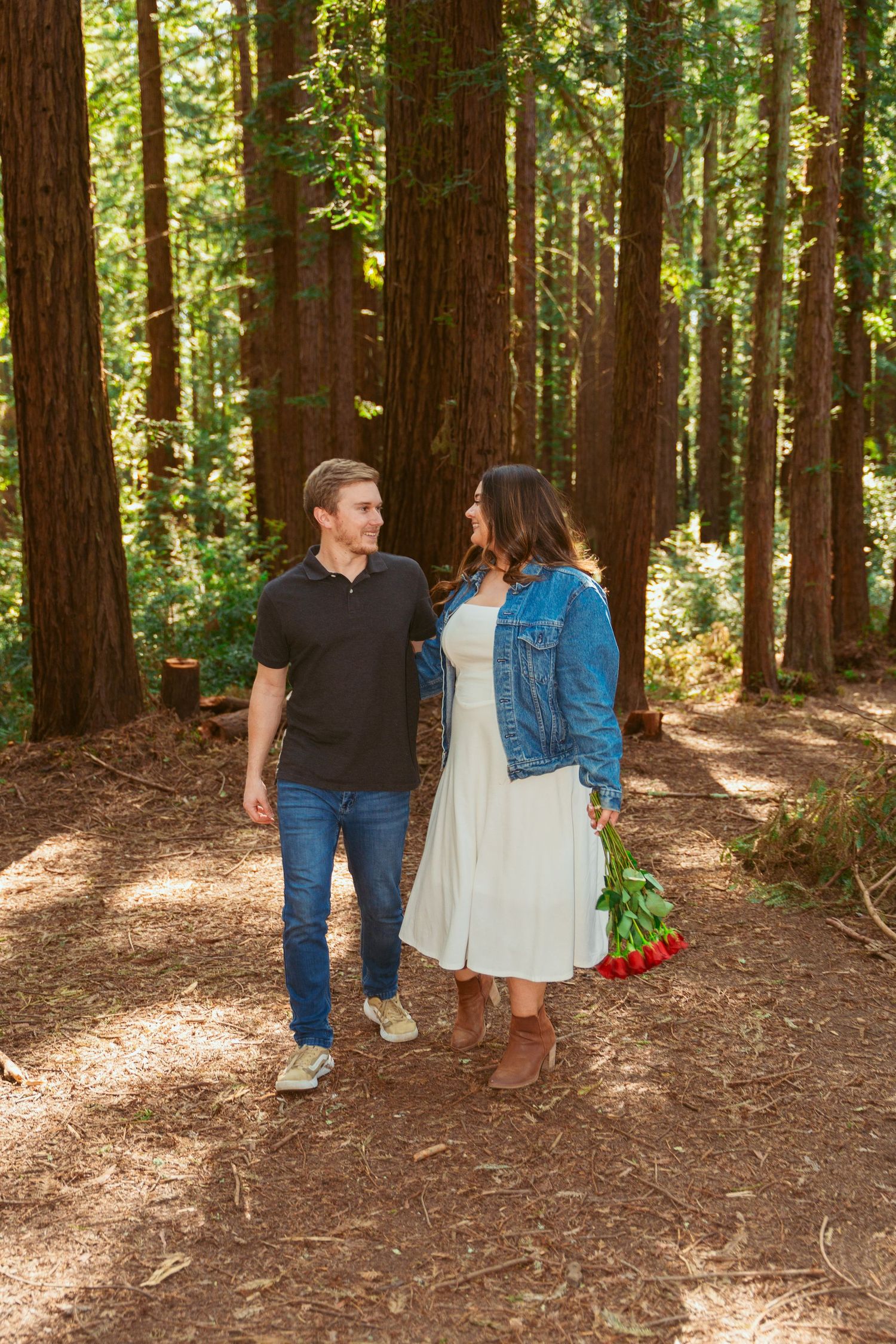 A couple walks hand in hand through a majestic redwood forest on a sunny day.