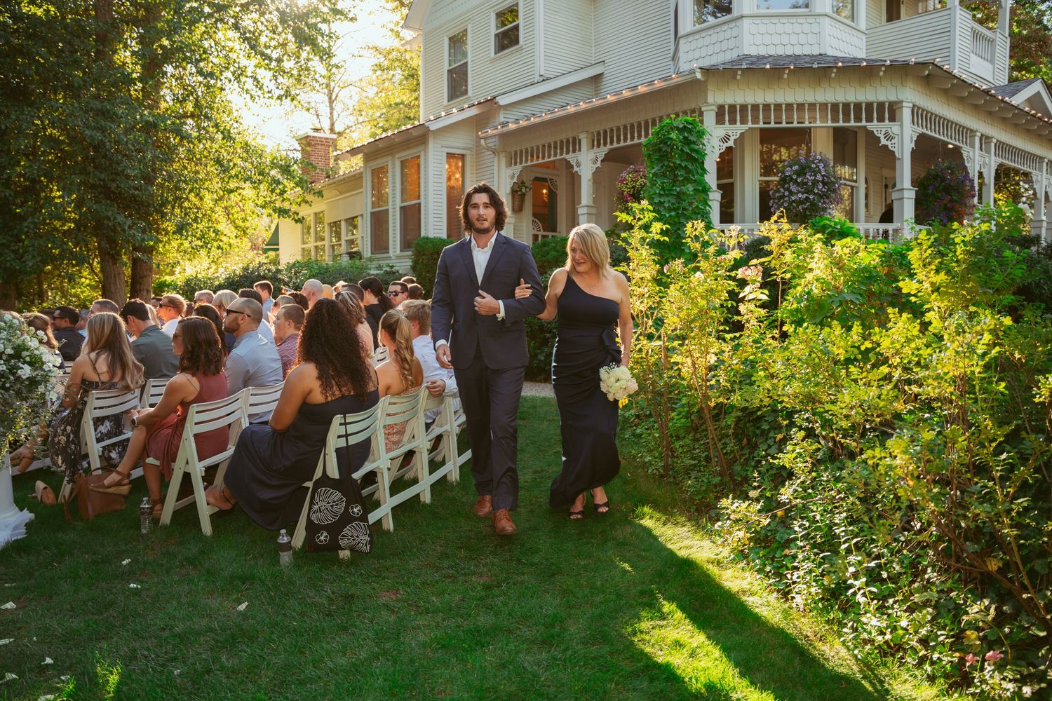 Wedding guests dance and celebrate outdoors on a lush green lawn during a summer garden reception.
