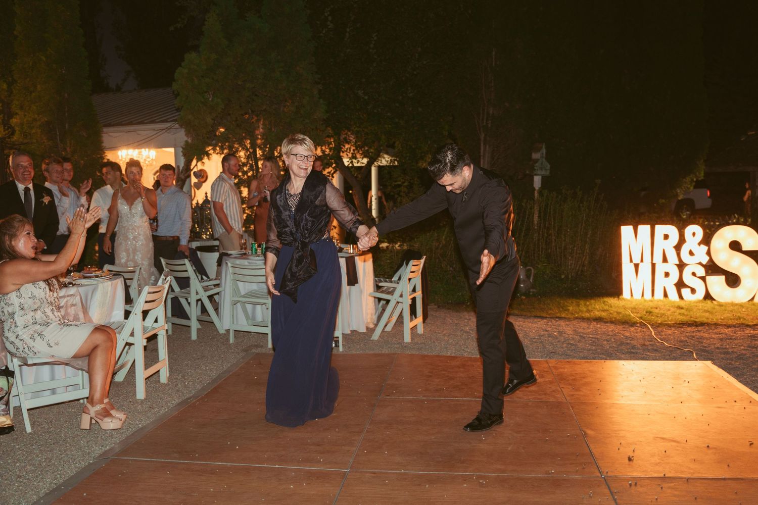 Outdoor wedding reception setup with illuminated signage and seating arrangements.