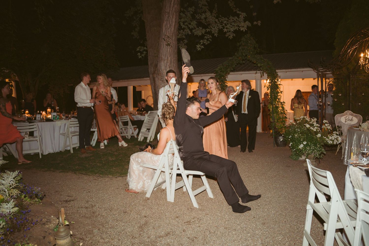 Wedding guests enjoying evening reception outdoors with white chairs and ambient lighting.