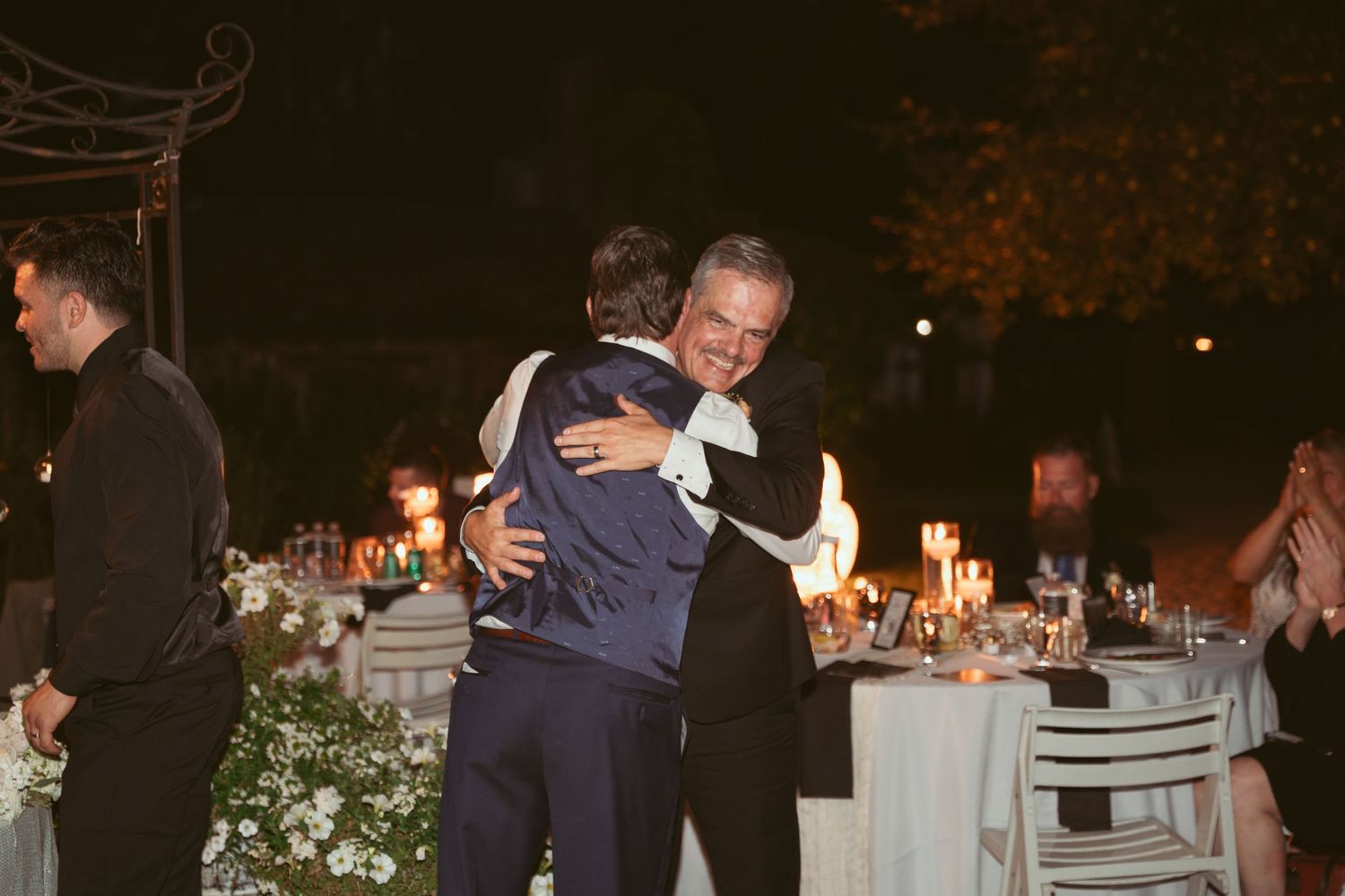 Wedding guests mingling and dancing during an evening celebration under a covered outdoor venue.