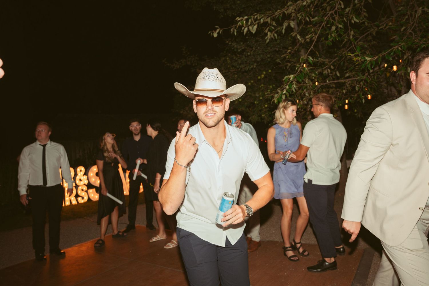Guest in cowboy hat enjoying drinks and dancing at outdoor wedding reception.