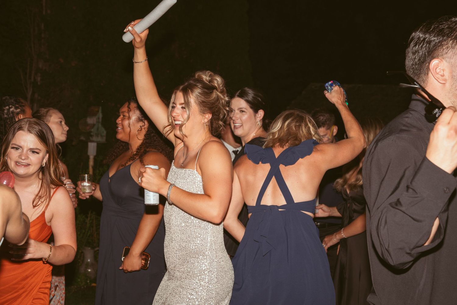 Crowd of wedding guests dancing with raised arms during a nighttime outdoor reception.