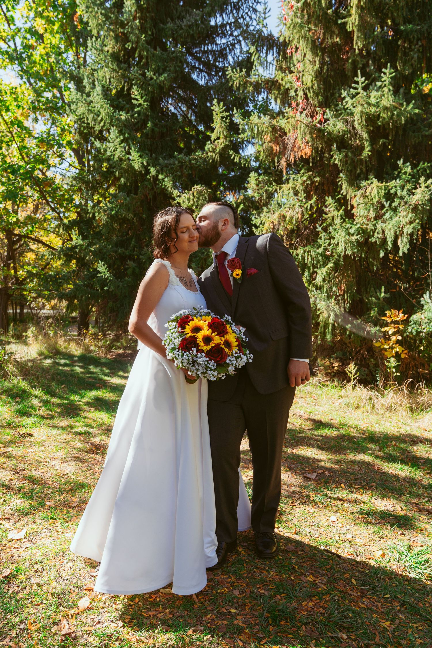 Newlyweds share intimate moment in sunlit garden setting with fall foliage.