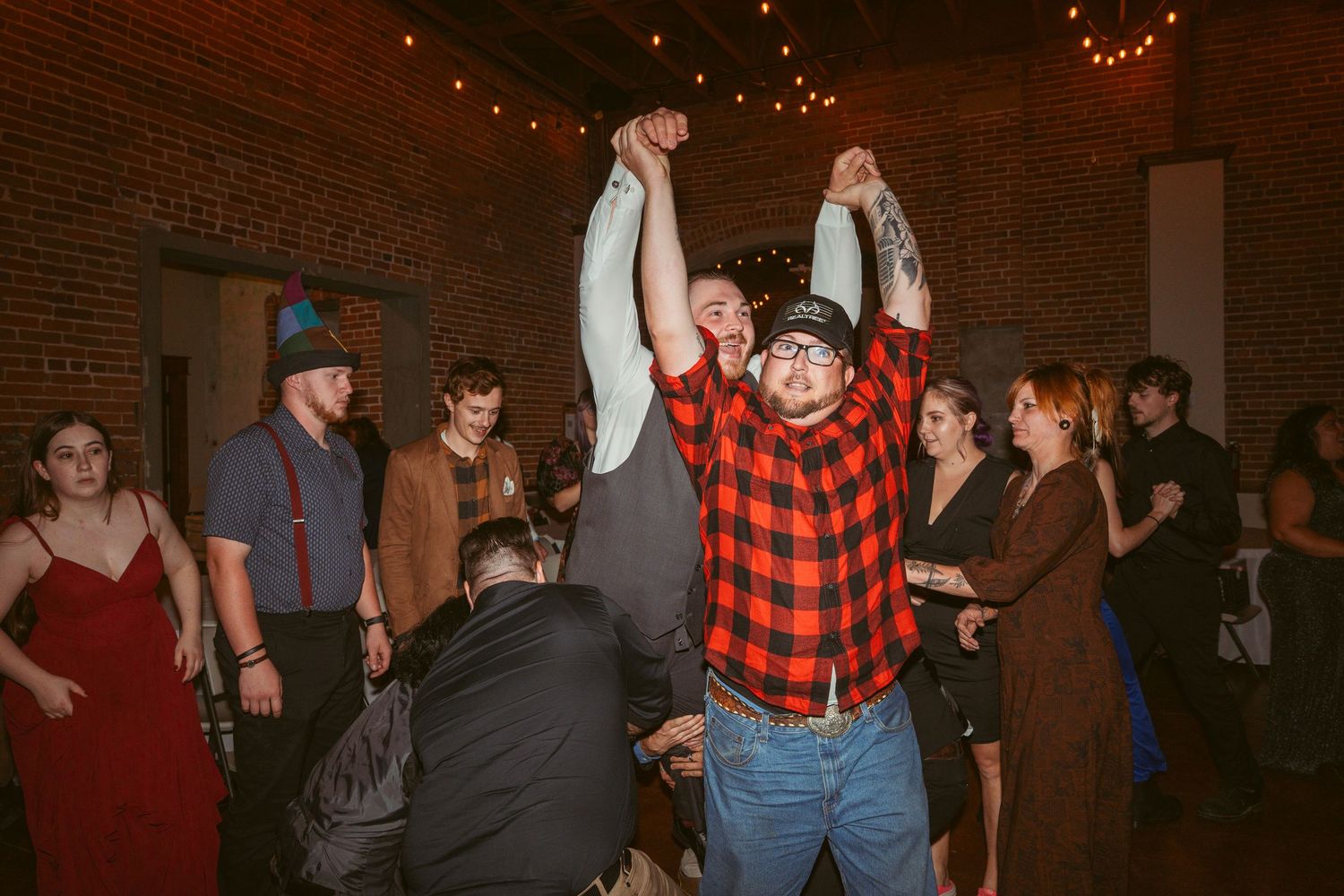 Celebratory crowd lifting someone up during a lively dance party under string lights.