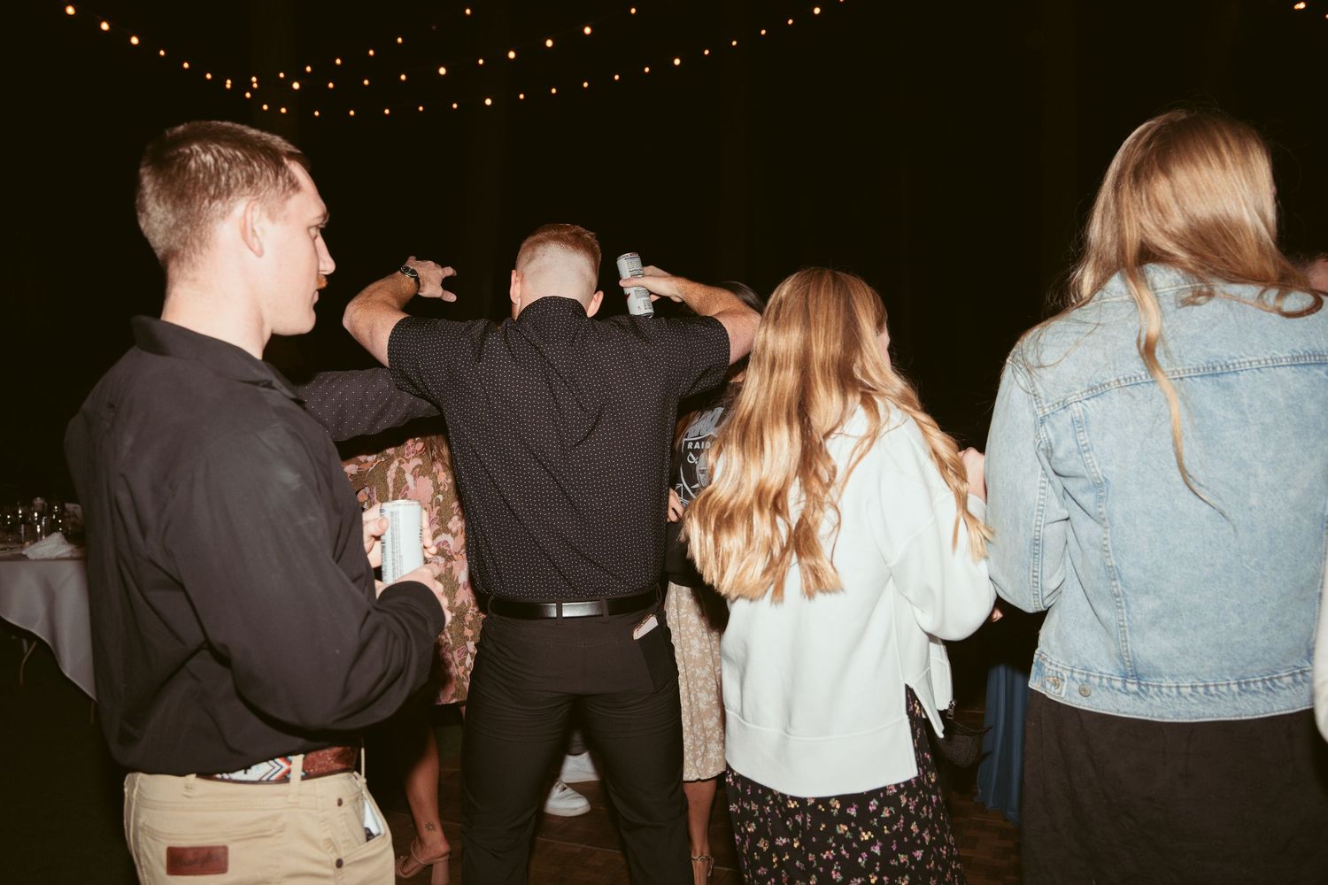 Group of guests socializing under decorative string lights at a nighttime gathering.